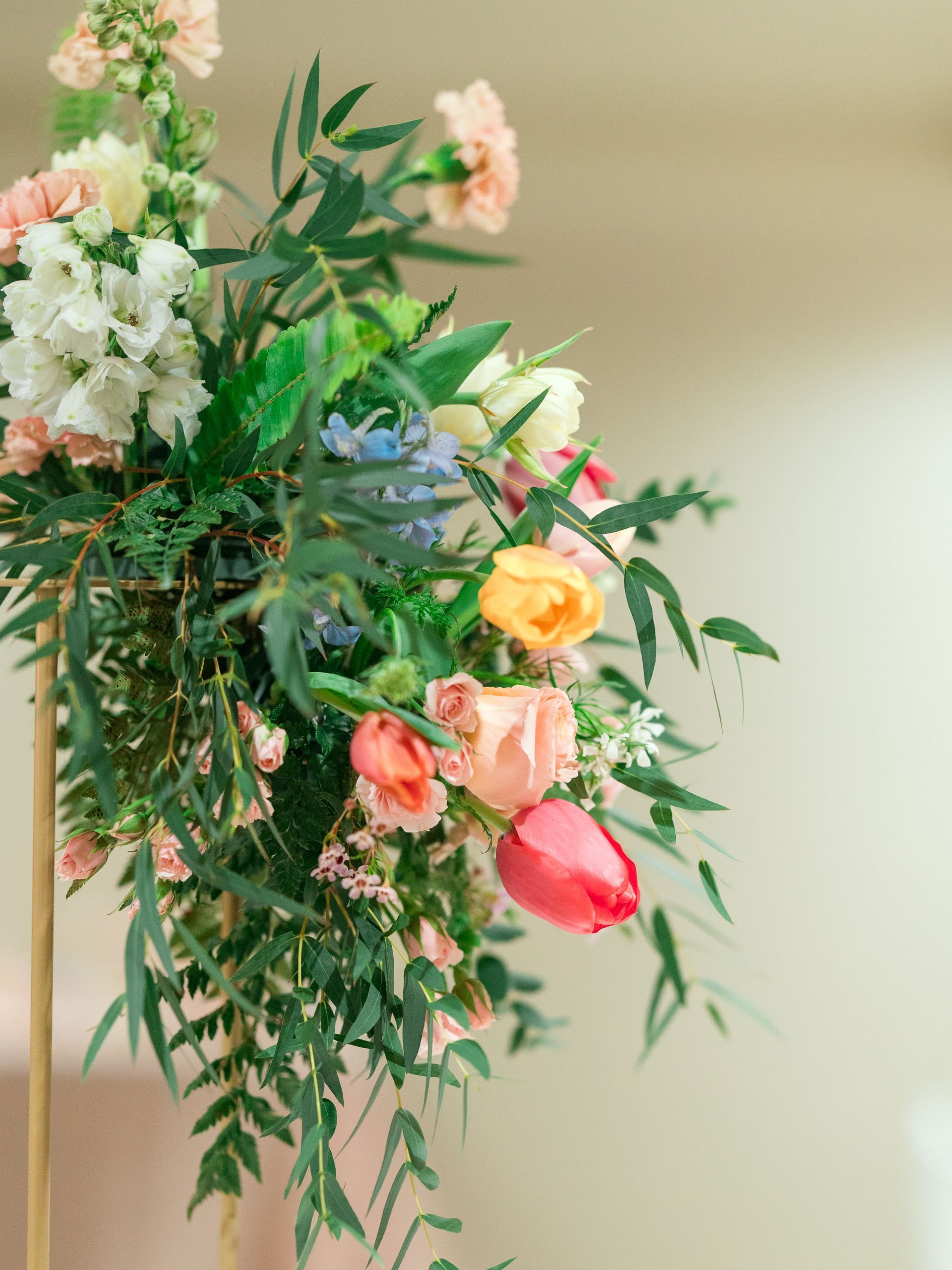 Floral arrangement with pink, yellow, and white flowers, green foliage, on a gold stand.