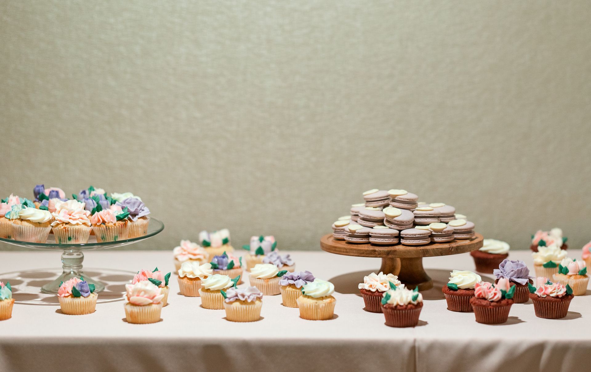 Dessert table with cupcakes and macarons, beige frosting, and floral decorations.