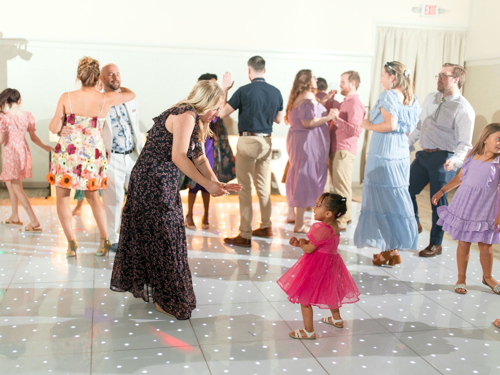 People dancing on a light-up dance floor. A young girl in a pink dress dances in the foreground.