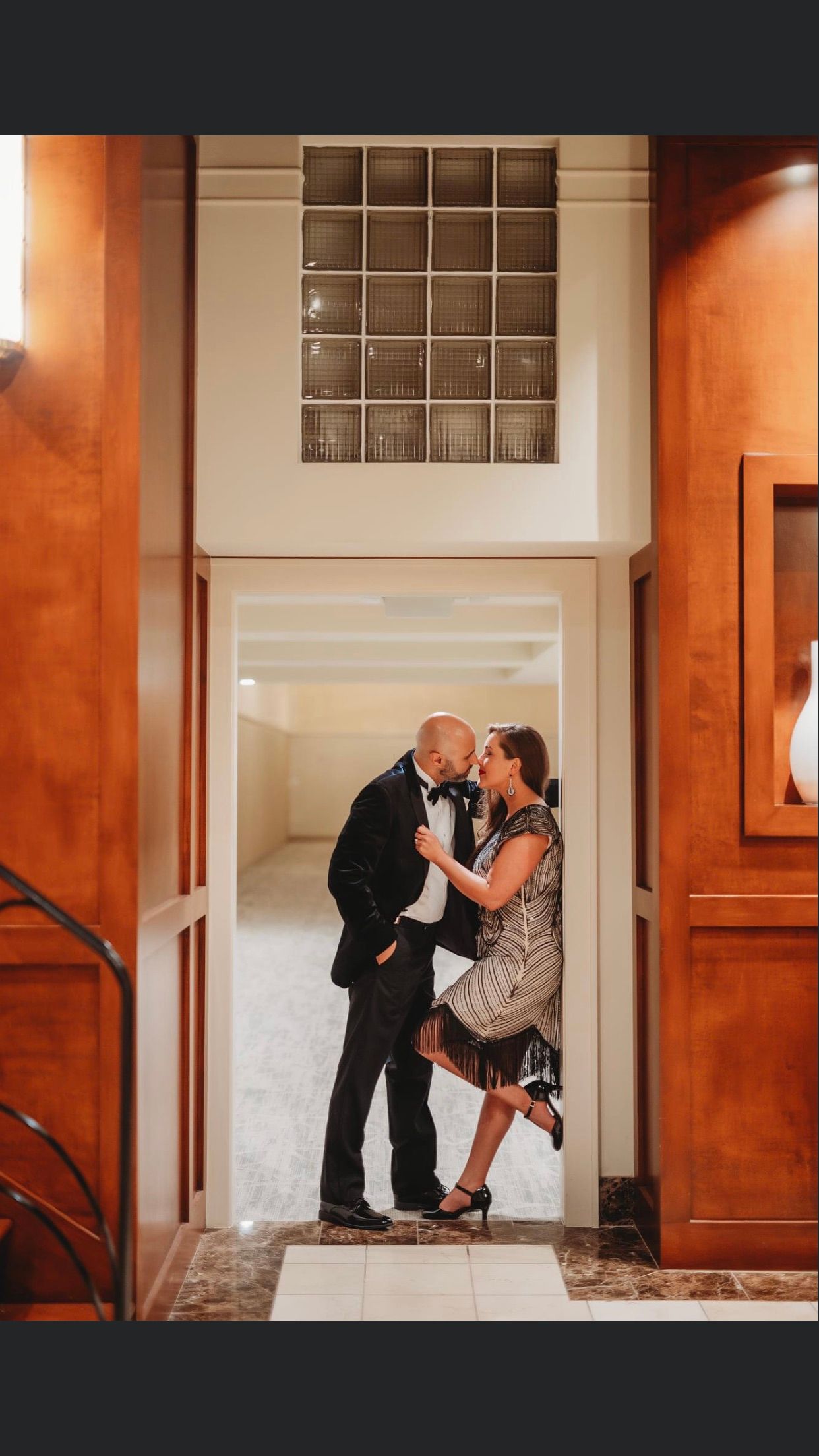 Couple kissing in doorway; woman in animal print dress, man in tuxedo, warmly lit interior.