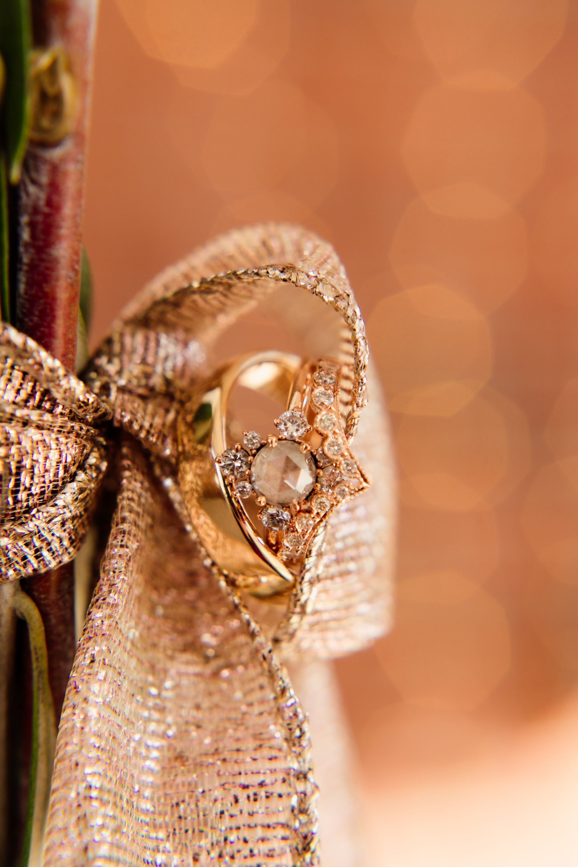 Gold wedding rings wrapped in shimmering gold ribbon, against an out-of-focus orange background.
