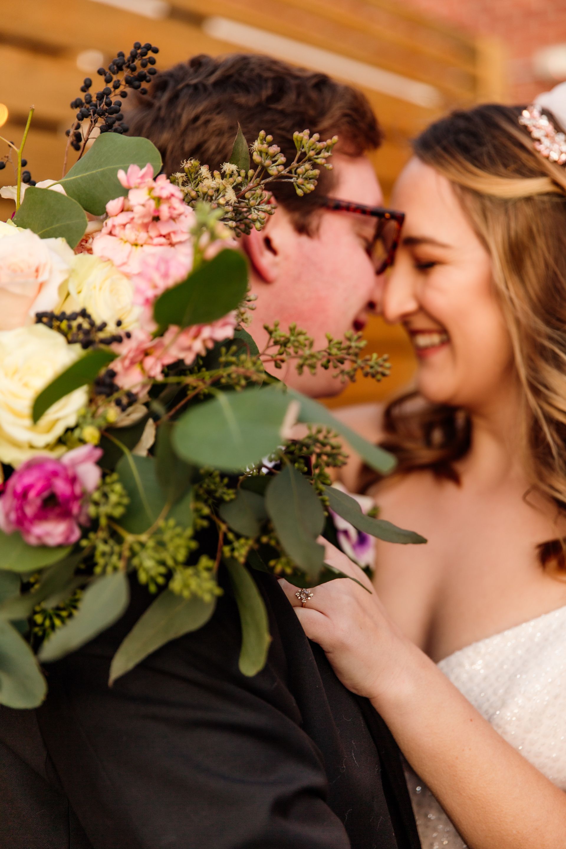 Bride and groom smiling close together, holding a bouquet. Outdoors, soft light.