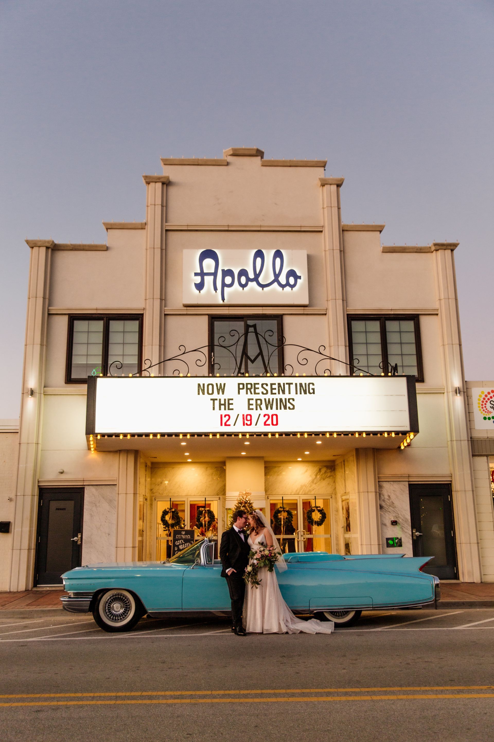 Bride and groom pose in front of the Apollo Theater with a blue vintage car.