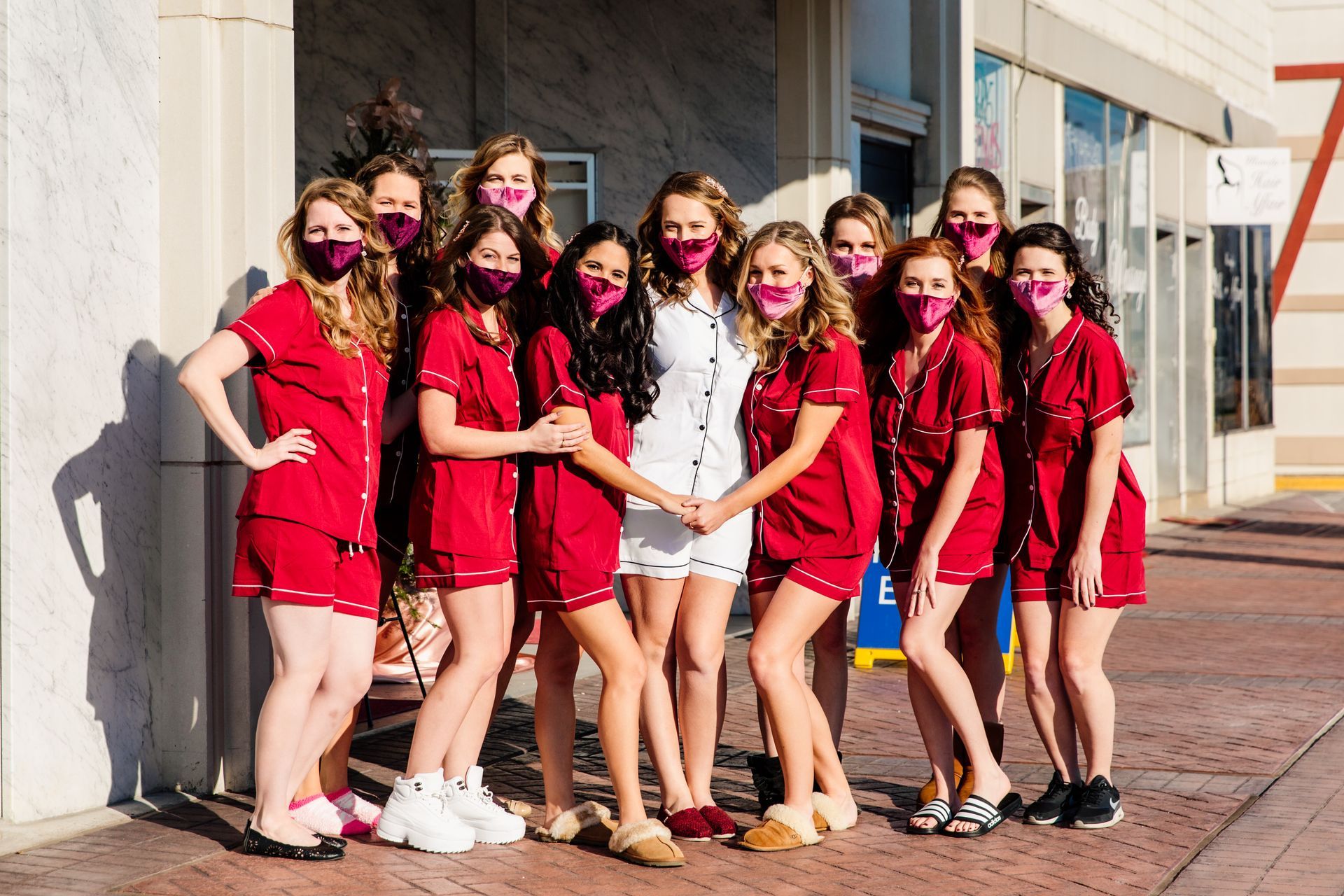 Group of women in red pajamas and masks, posing outside a building.