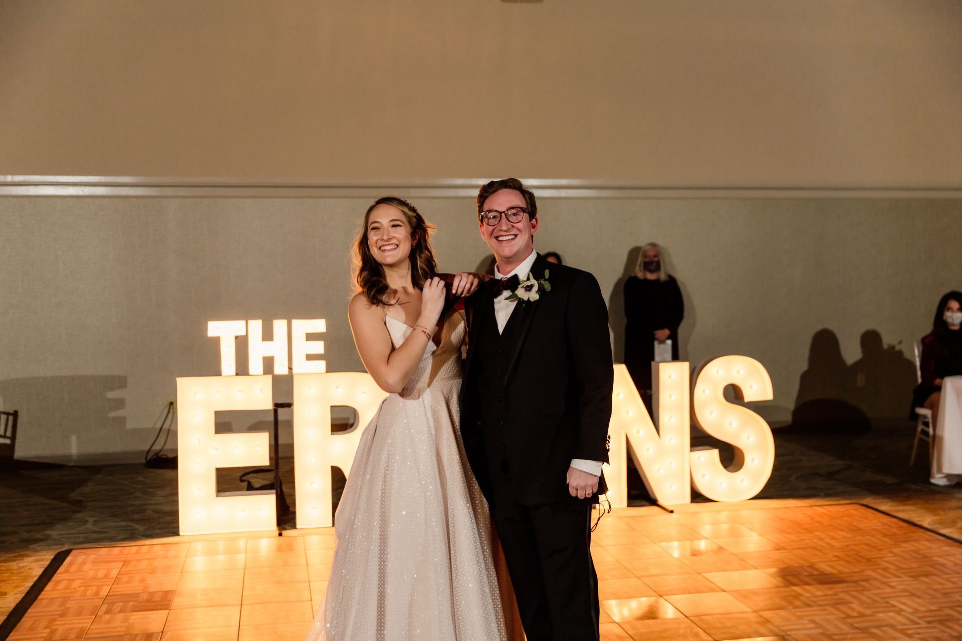 Bride and groom stand on a dance floor in front of illuminated 
