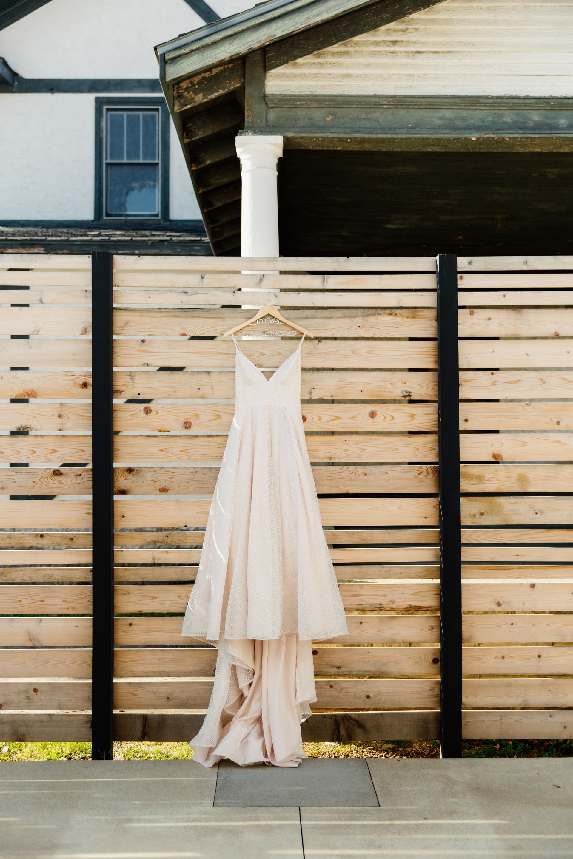 Wedding dress hanging on a wooden fence outdoors, ivory with a train, sunny day.