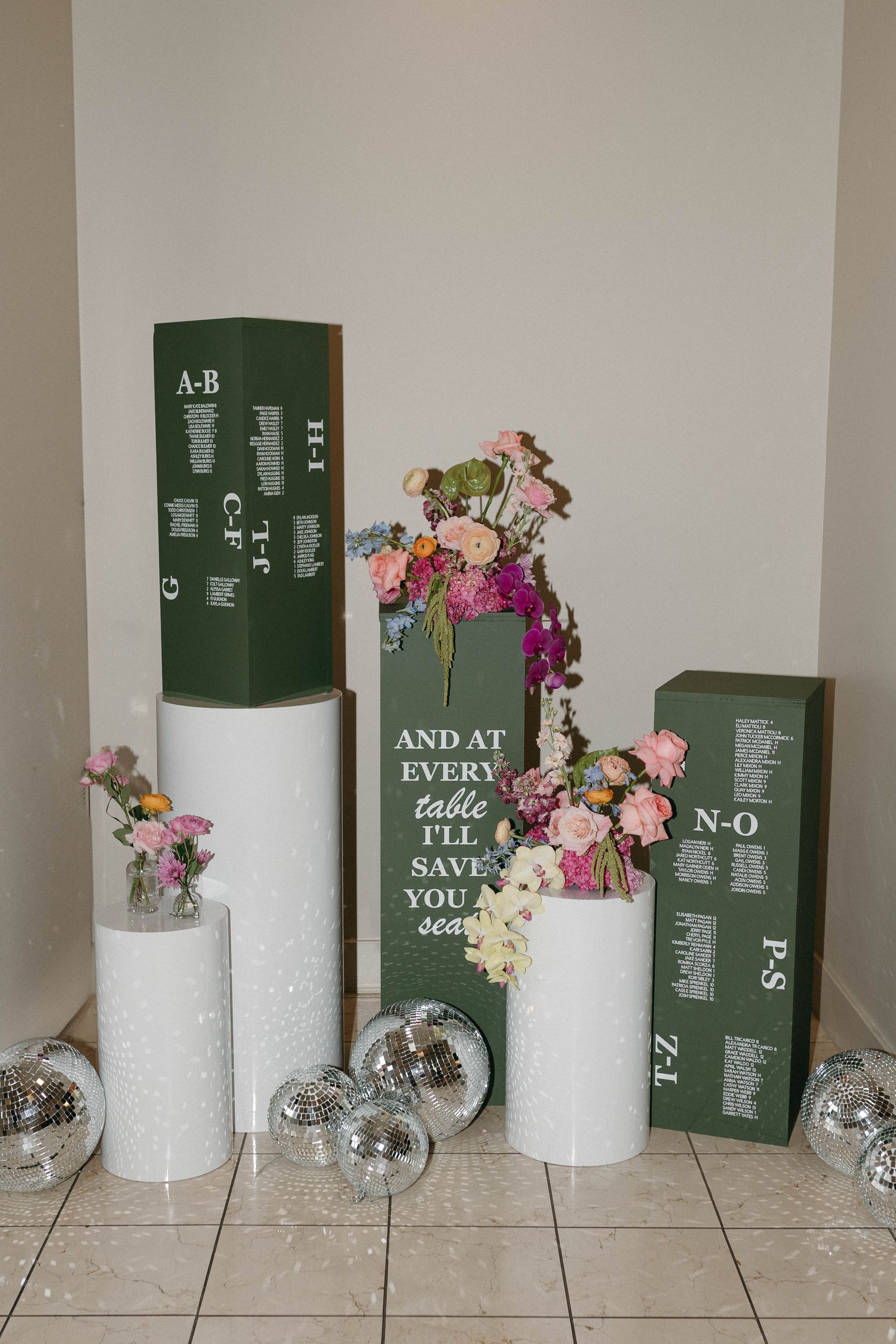 Display of flowers on white and green pedestals, with disco balls.