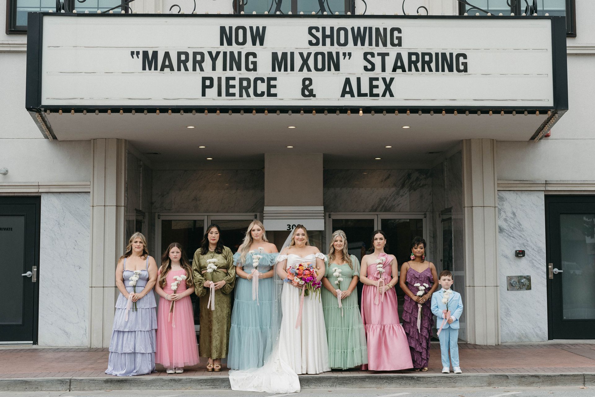 Bridesmaids and a young boy pose in front of a theater marquee reading 