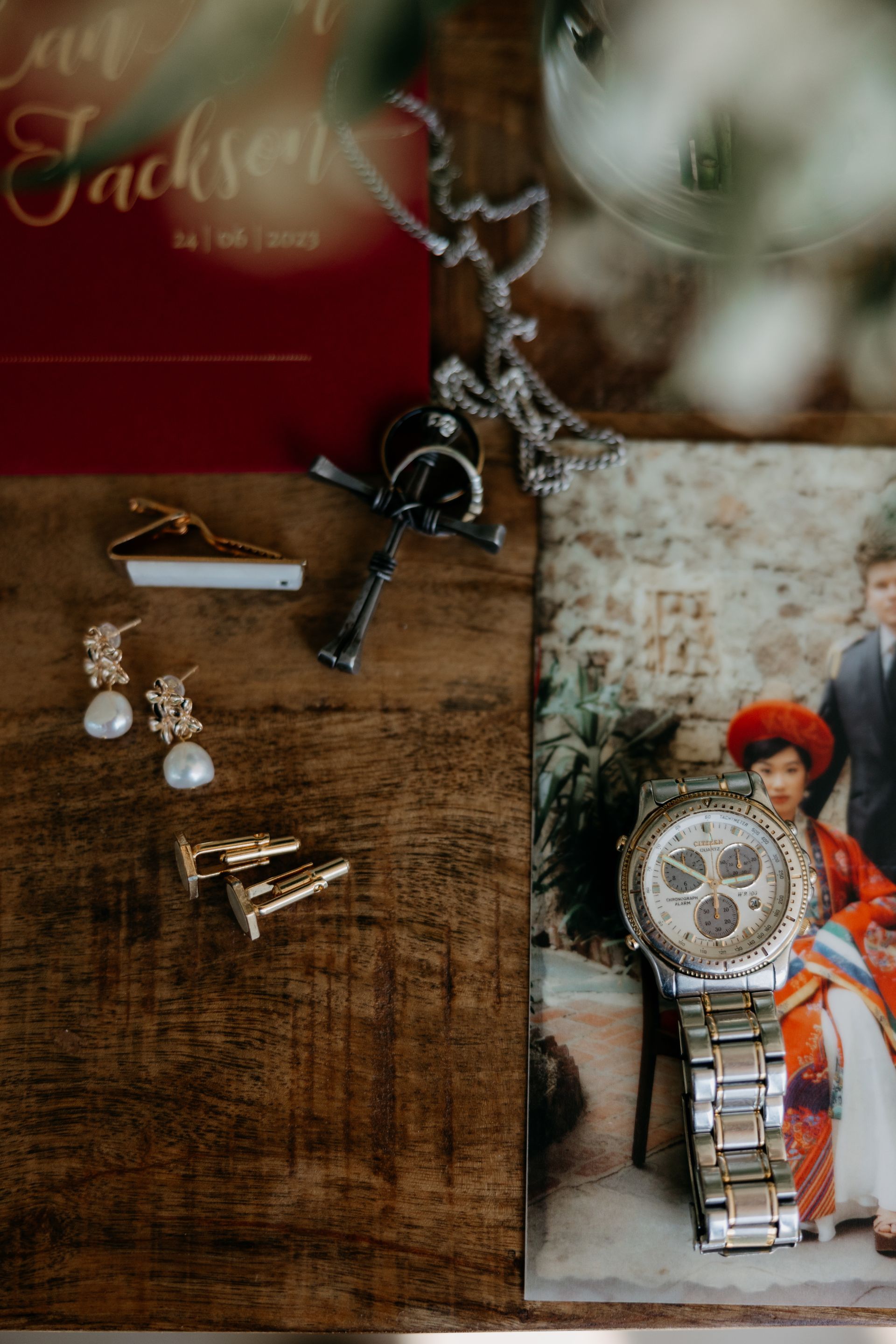Wedding accessories on a wooden surface: invitation, watch, necklace, earrings, cufflinks, and photo of a couple.