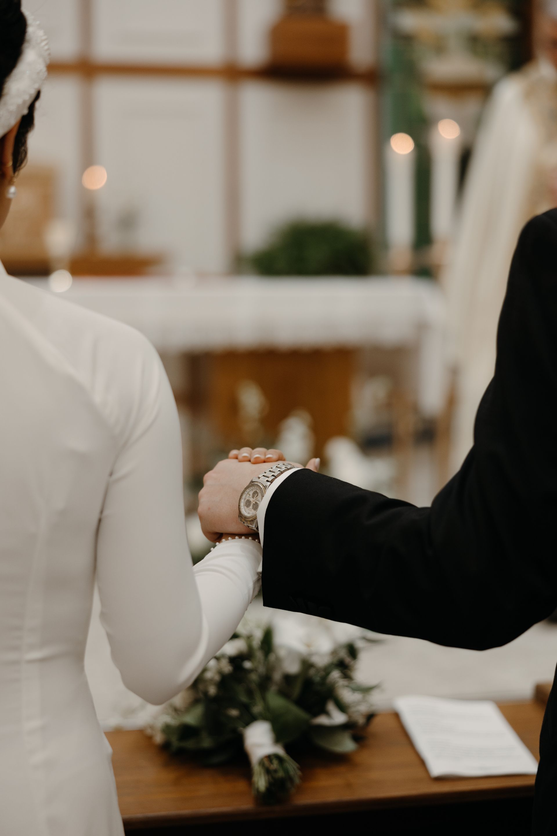 Bride and groom holding hands during a wedding ceremony in a church. Bouquet on a table.