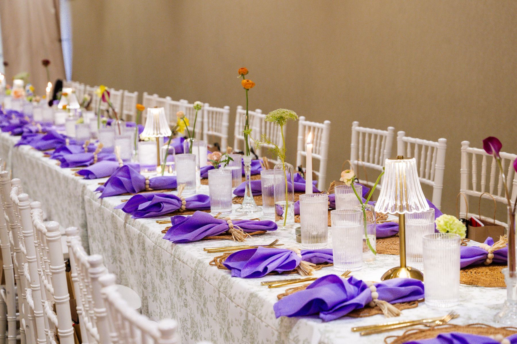 Long table set for a formal event with purple napkins, gold chargers, and white chairs.