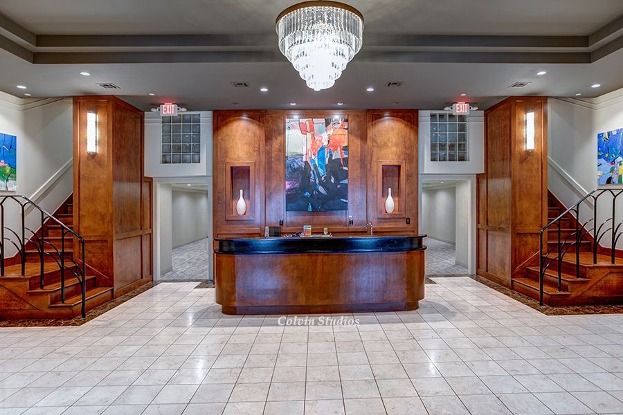 Lobby with reception desk, elevators, staircase. Wood paneling, chandelier, art on the wall, and tiled flooring.