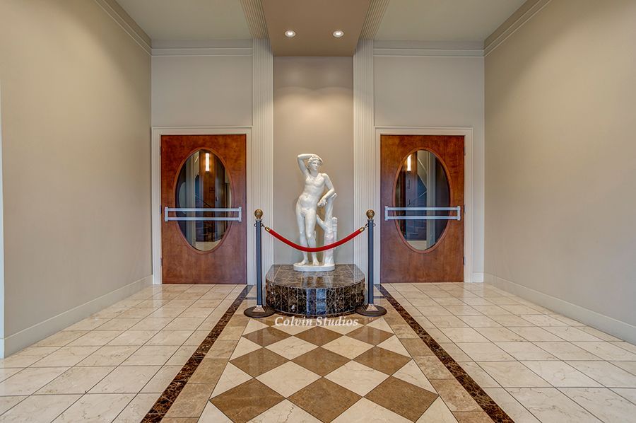 Hallway with statue between two wooden doors, checkerboard floor, and rope barriers.