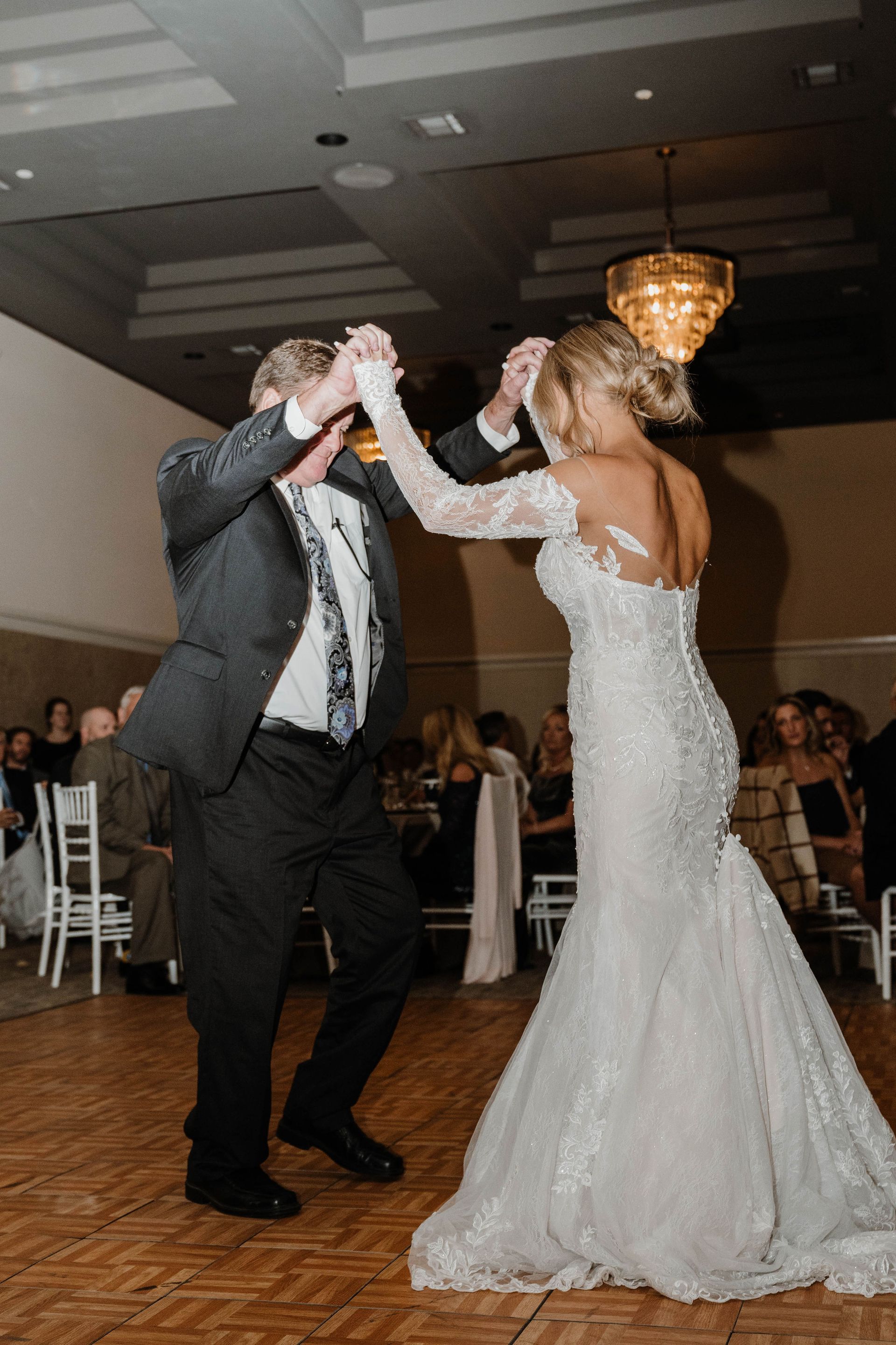 Bride and groom dance at reception; bride in white gown, groom in gray suit.