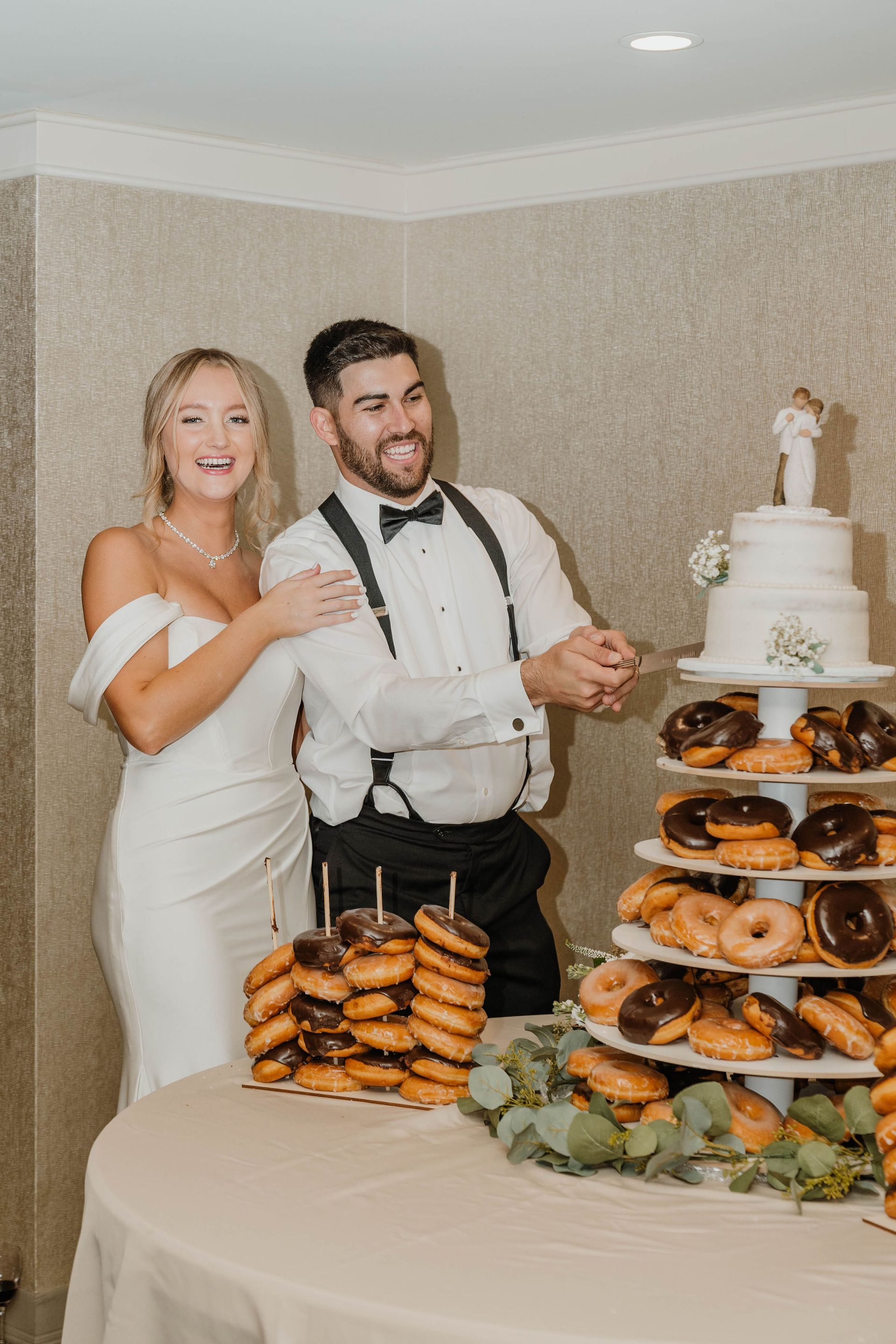 Bride and groom cutting wedding cake at reception, donut tower, smiles.