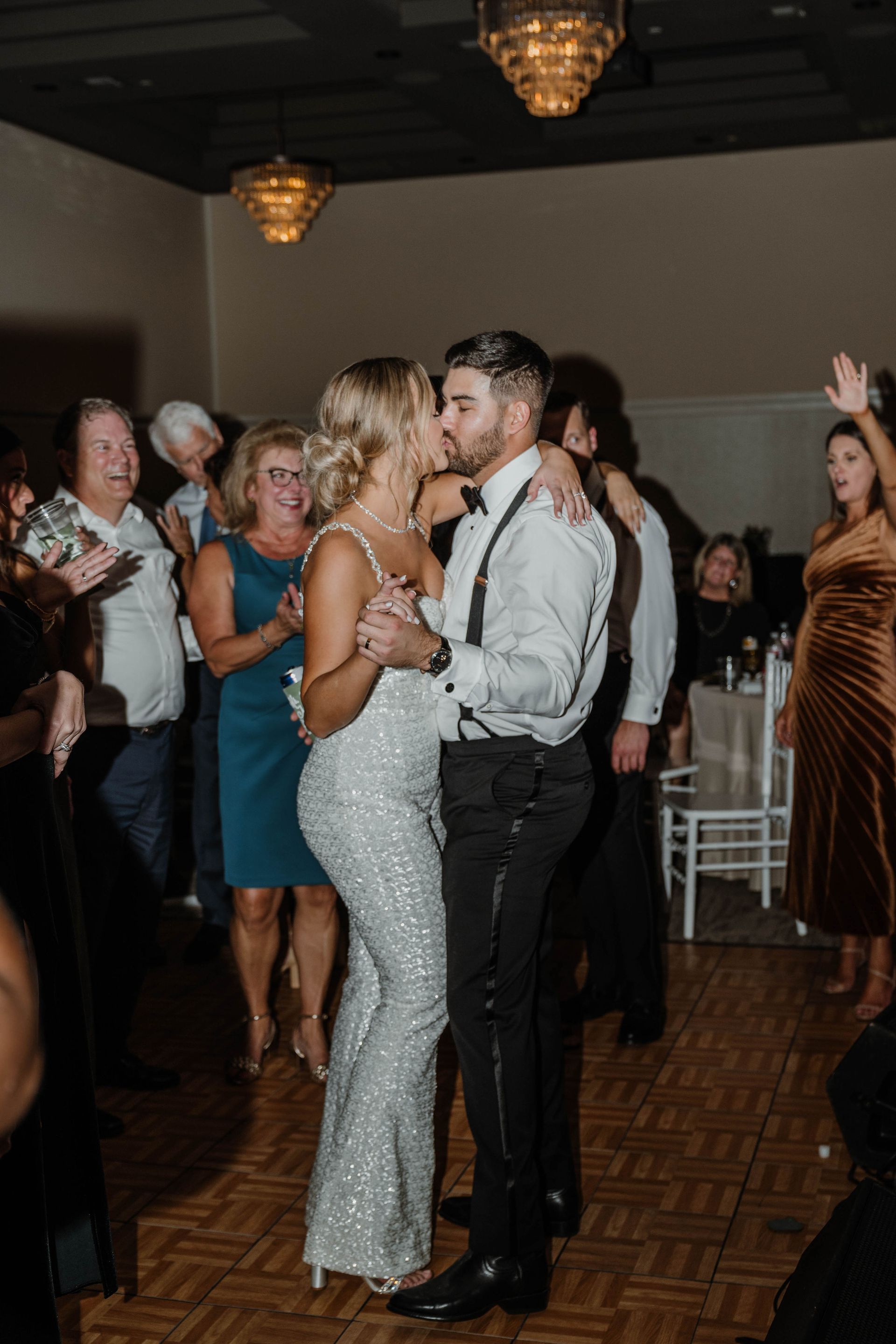 Couple dancing at a wedding reception, nearly kissing. Guests watch, some clapping.