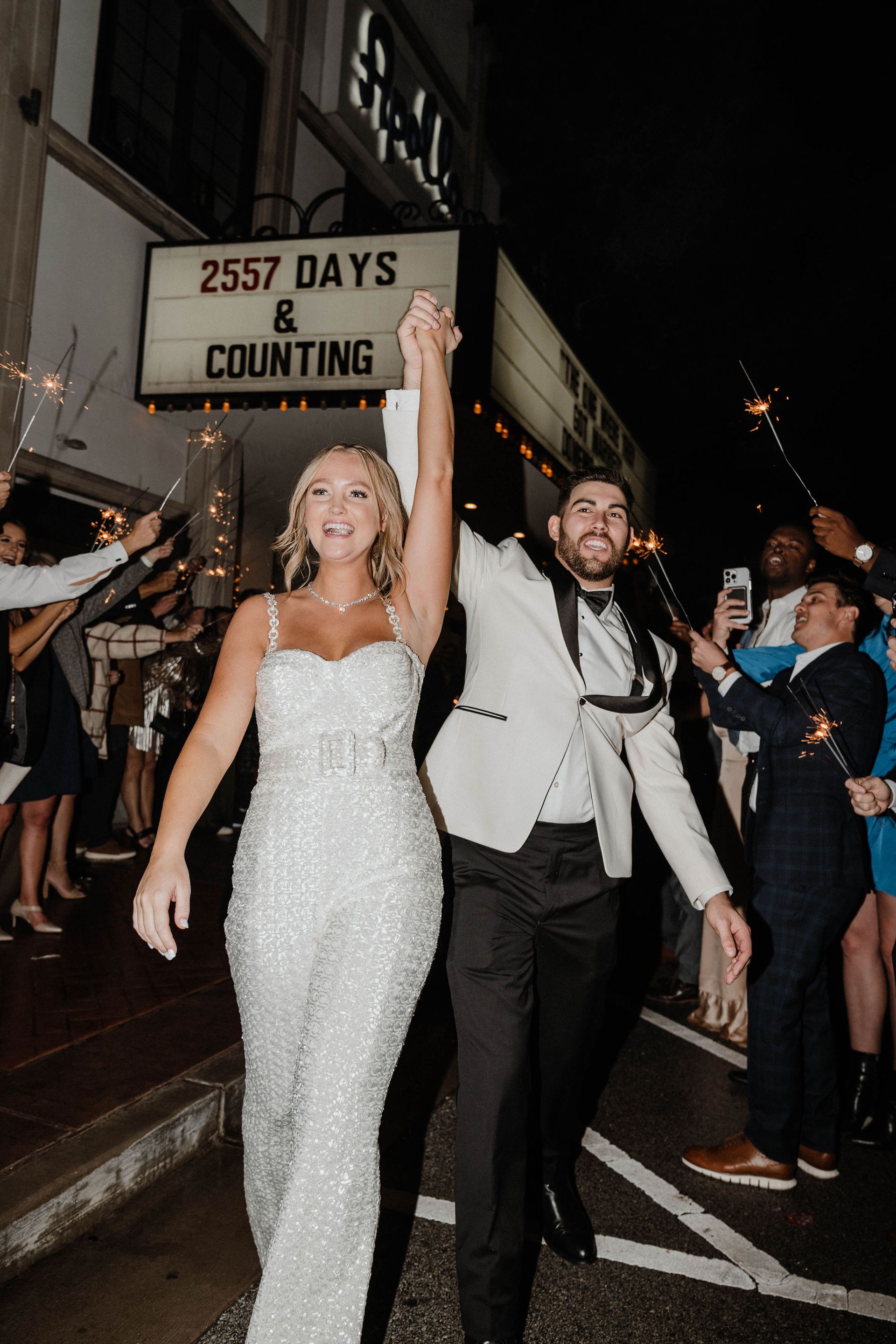 Newlyweds holding hands, exiting venue beneath sign reading 
