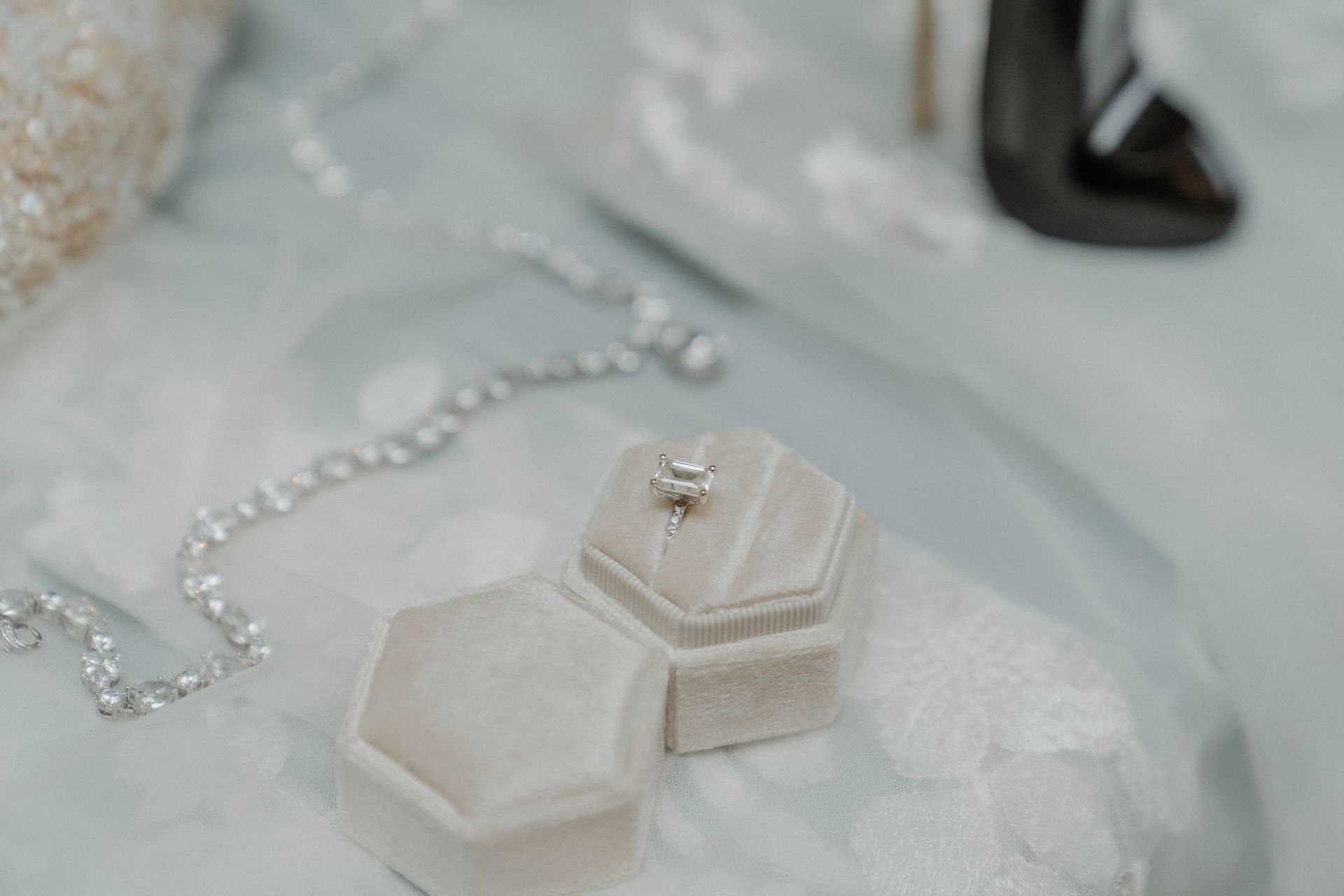 Diamond engagement ring in a velvet box, with a necklace and a shoe on a light blue surface.