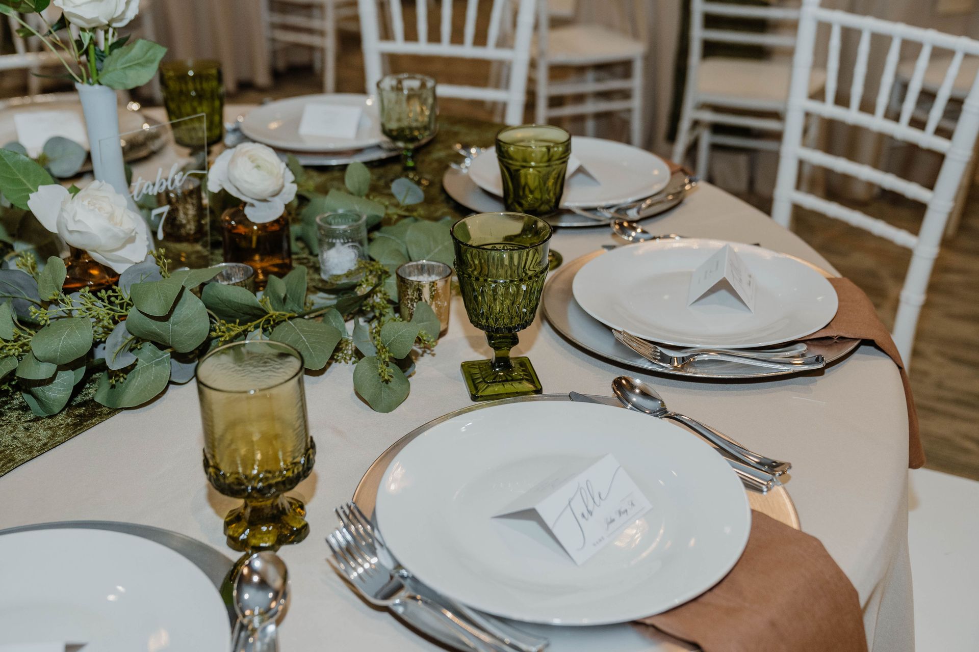 Formal table setting with white plates, green glasses, and floral centerpiece.