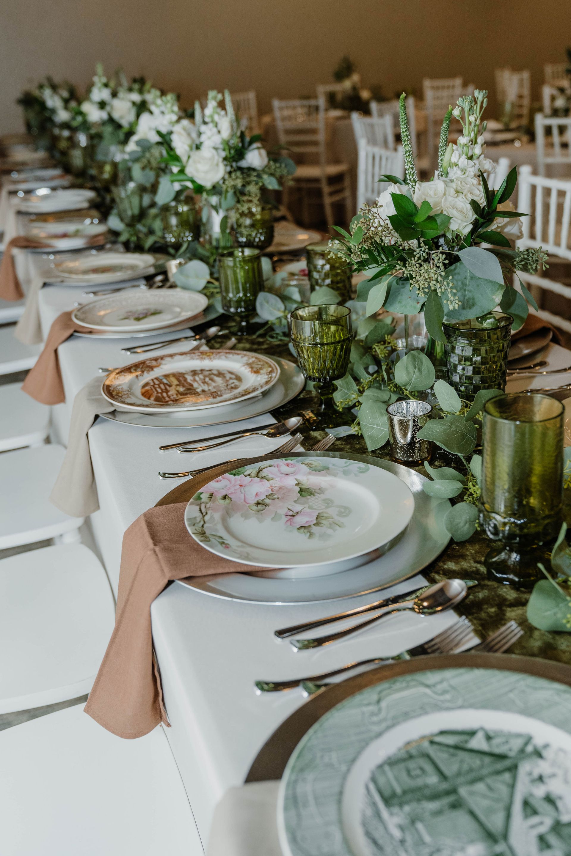Elegant wedding reception table setting with floral centerpieces, vintage plates, and glassware.