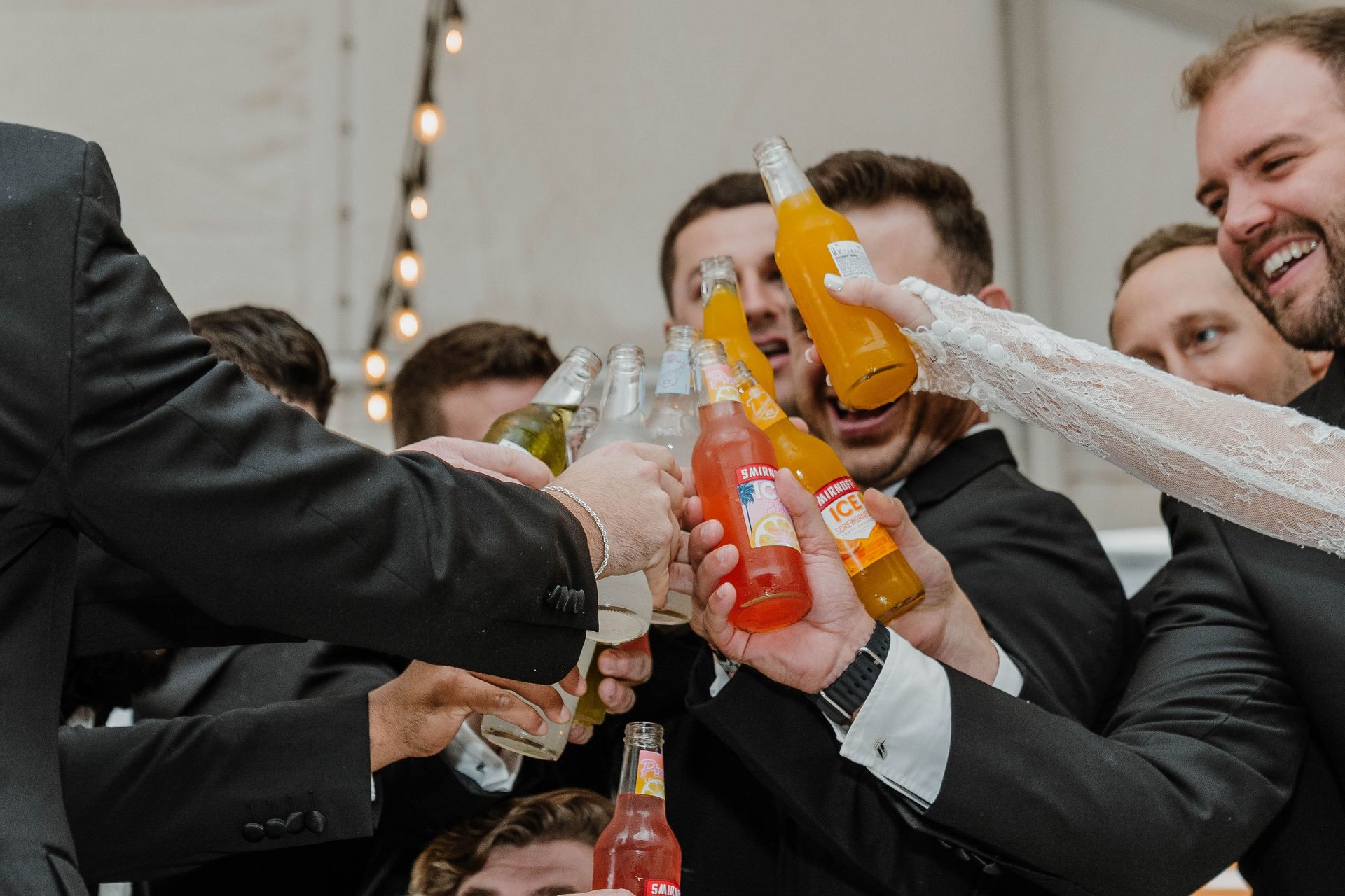 People in suits toasting with bottles of soda; celebratory gathering indoors.