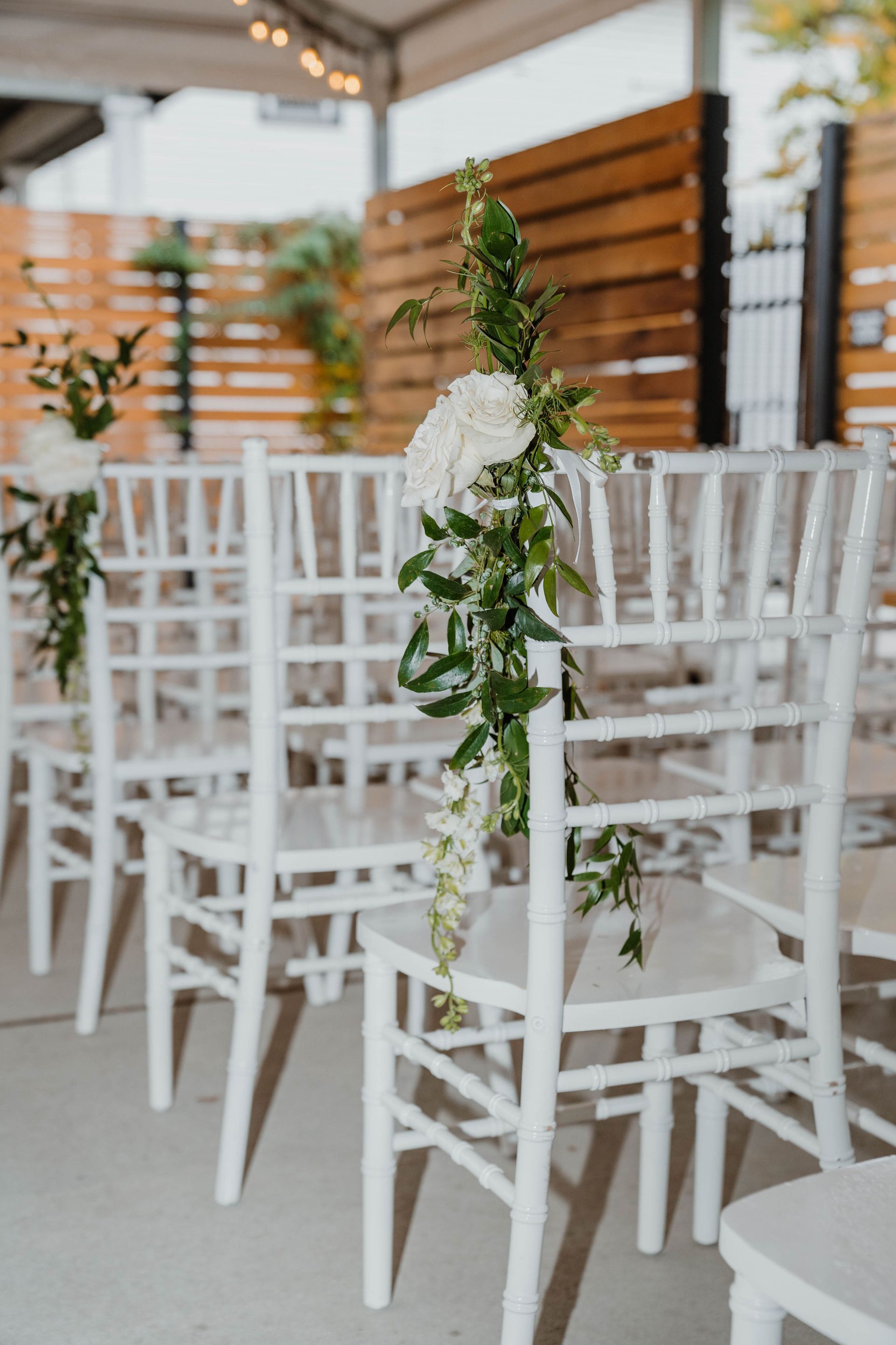 White chairs decorated with flowers for an outdoor wedding ceremony.