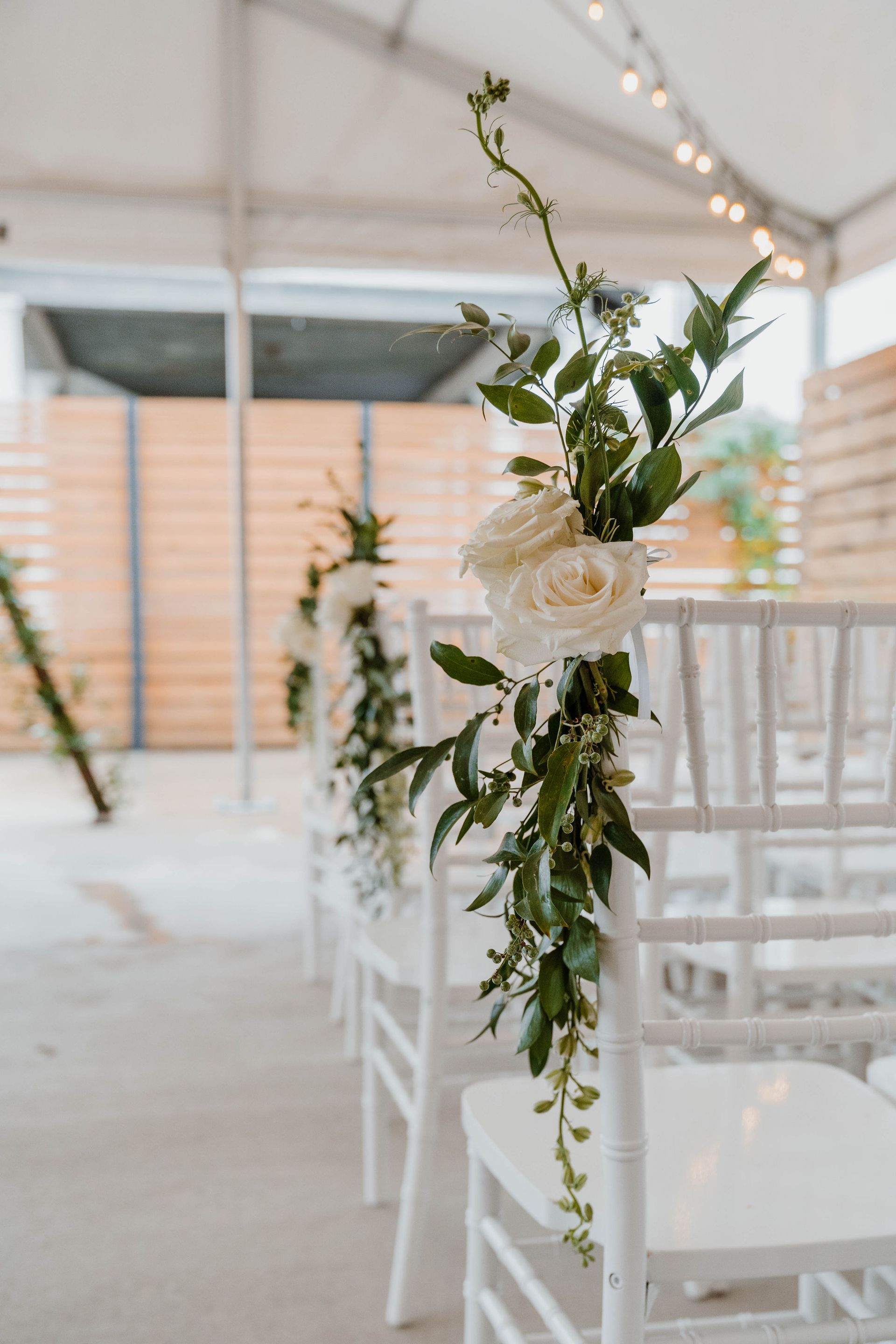 White chairs decorated with flowers line an outdoor event space.
