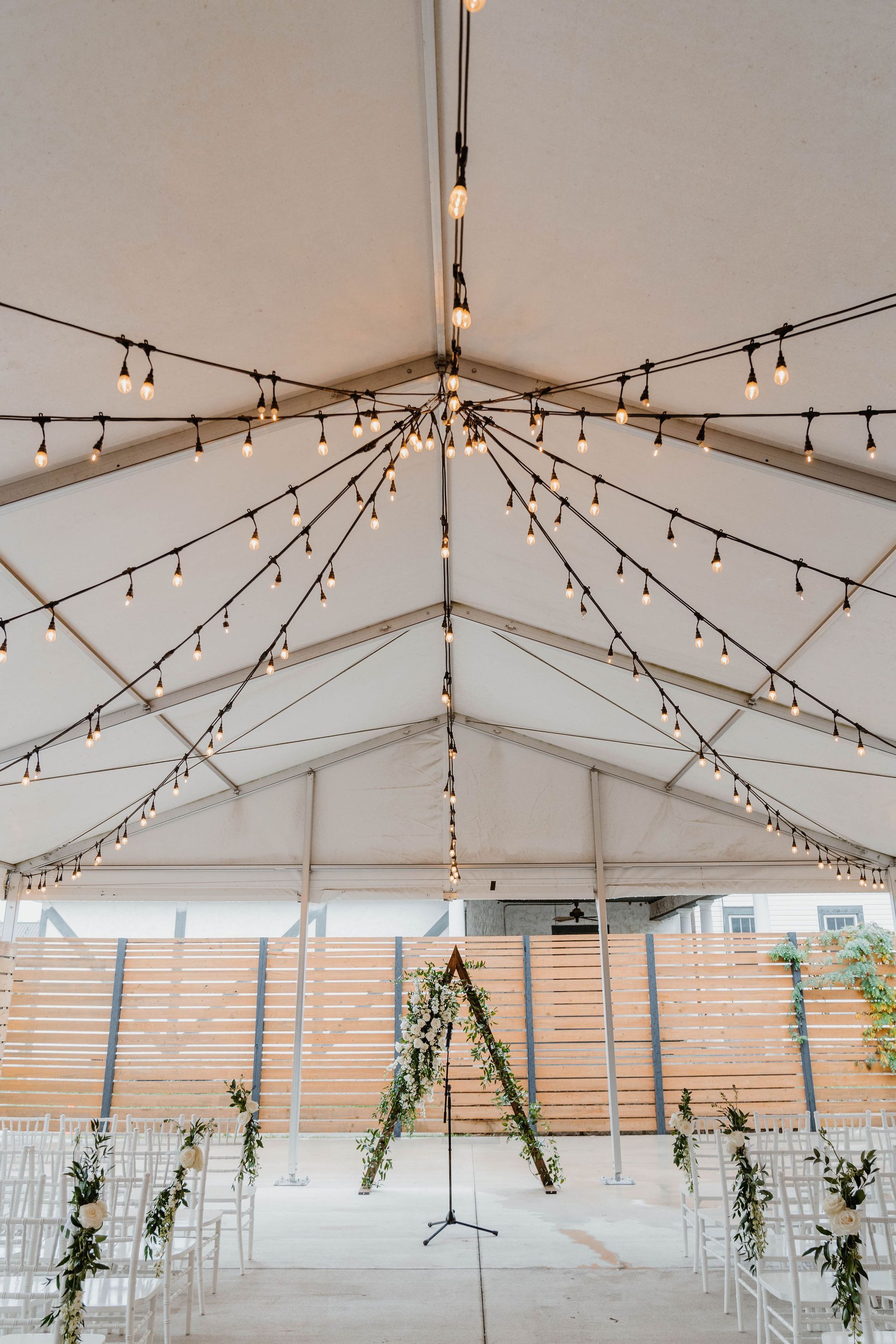 Wedding ceremony setup under a tent with string lights and floral decorations.