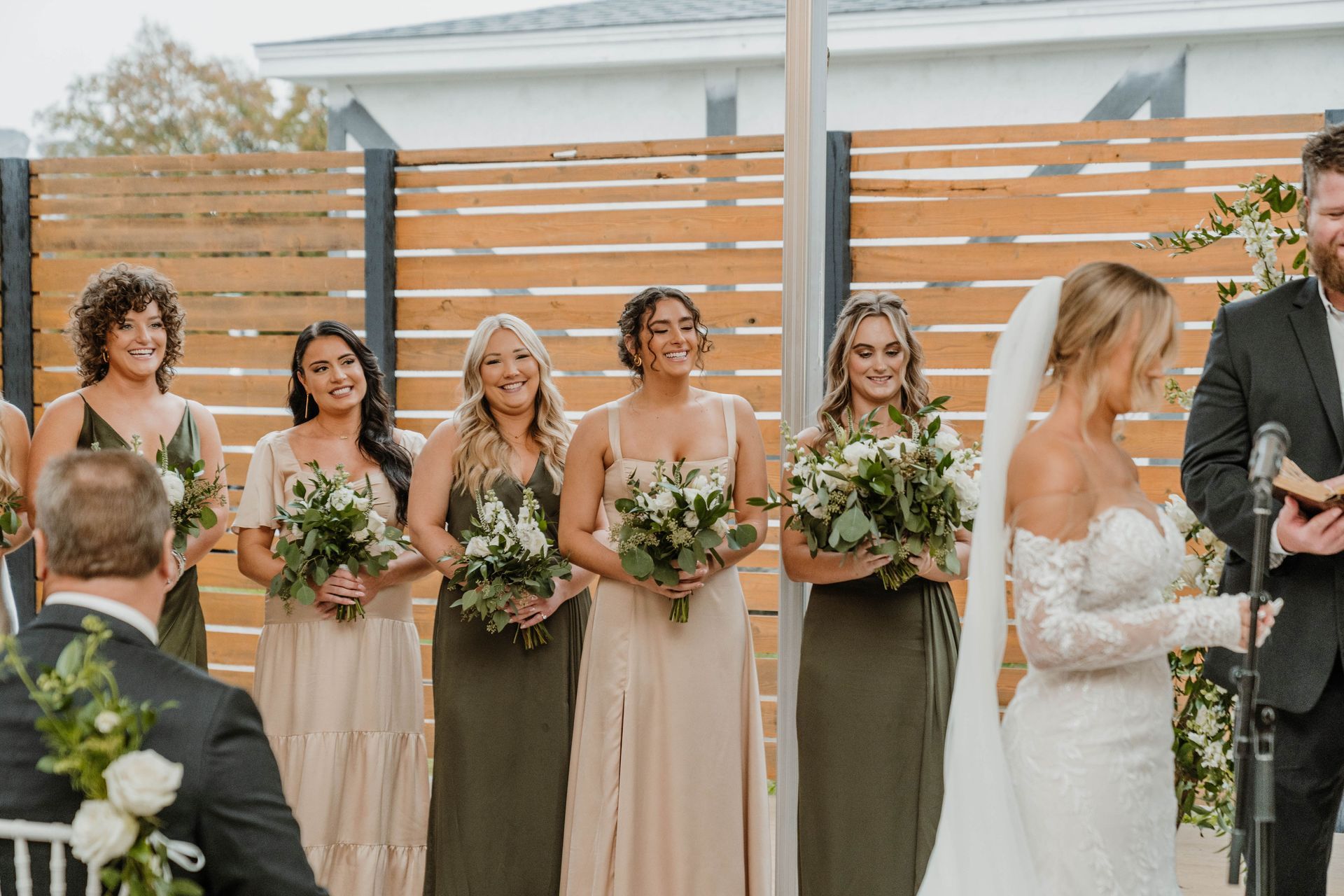 Wedding ceremony: Bride and groom exchanging vows, bridesmaids in olive green and beige dresses, outdoor setting.