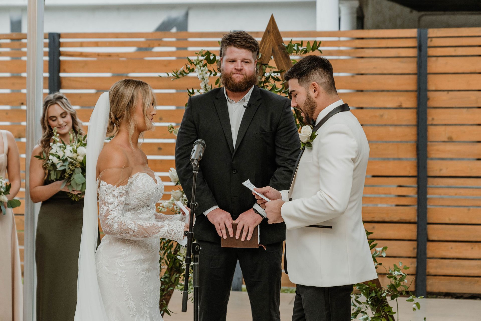Wedding ceremony with a bride and groom, officiant, and bridesmaid. The bride wears a white dress; the groom, a white suit.