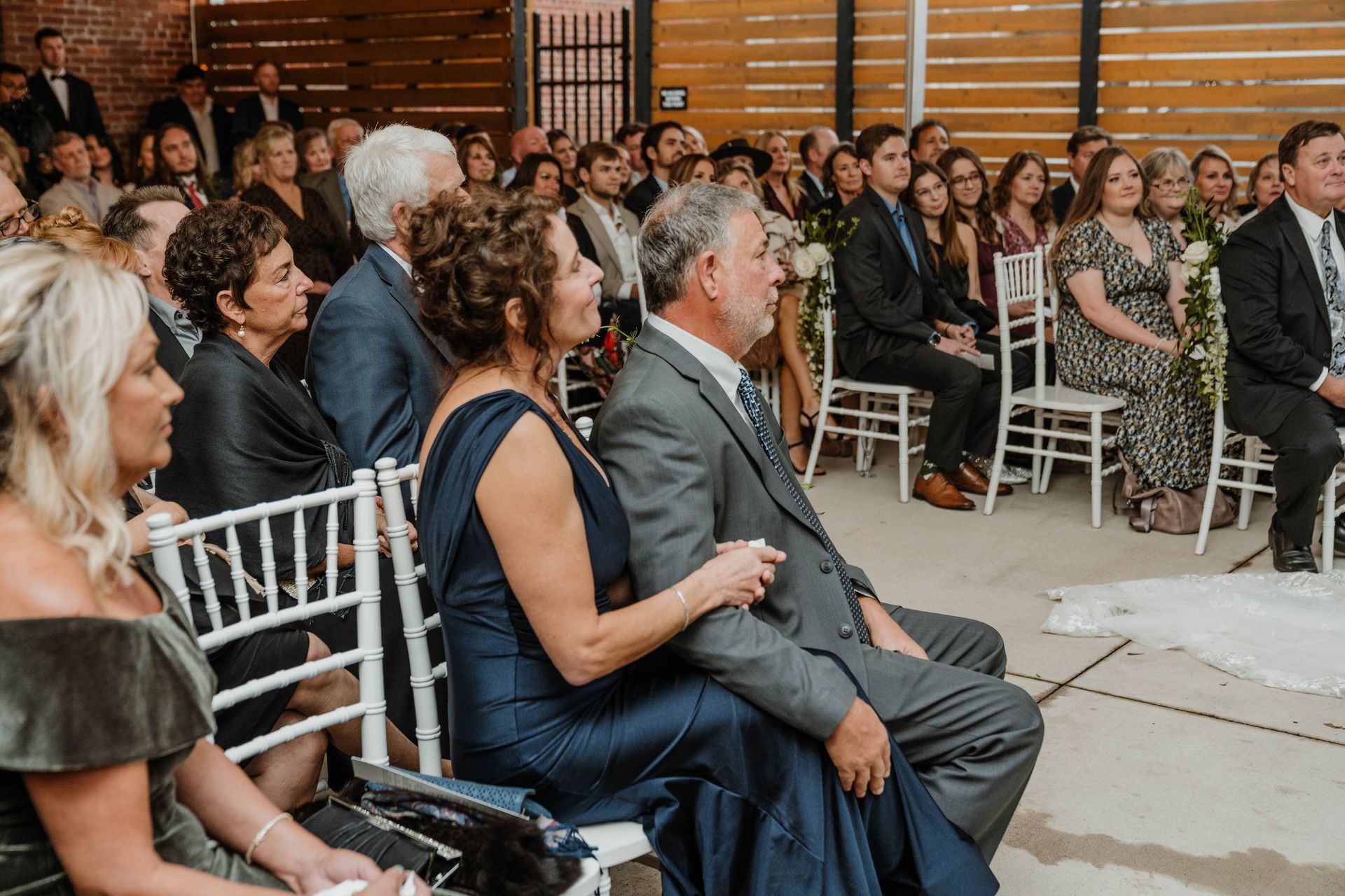 Wedding guests seated outdoors, watching the ceremony. Some are looking forward, others have turned to the side.