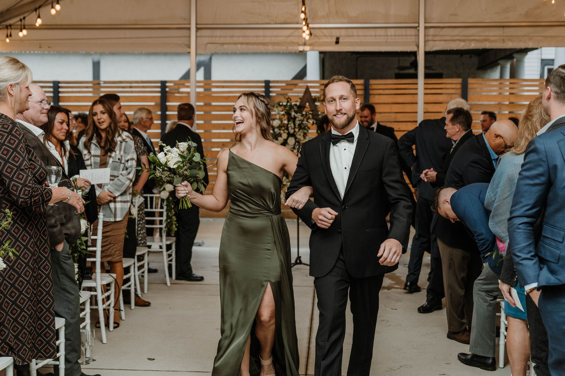 Wedding recessional: Couple, in formal wear, walking down aisle with guests. Green dress, black tux.