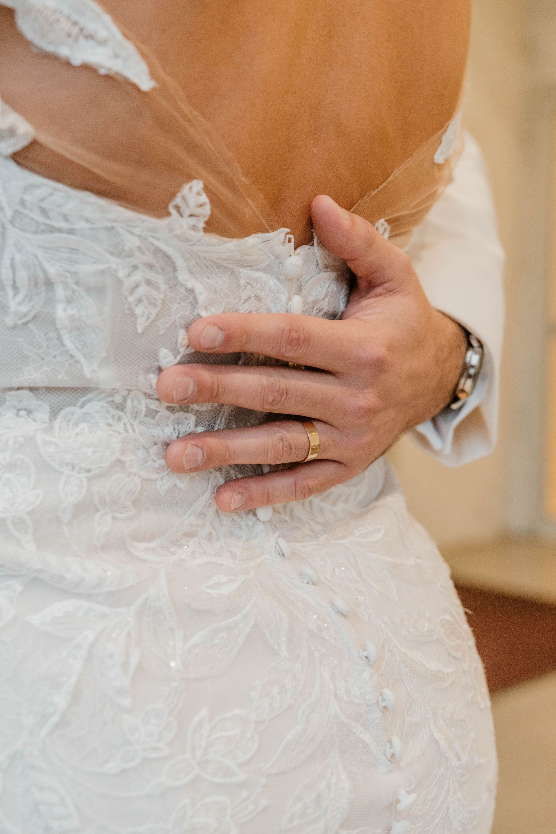 Hand with wedding ring on a bride's back, adjusting her dress.