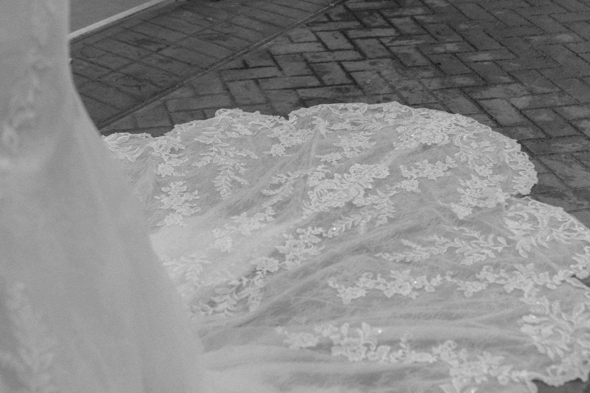 Close-up of a white lace wedding dress on a brick-paved surface.
