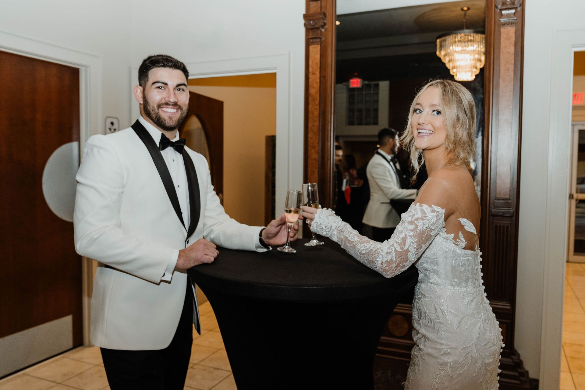Couple toasting glasses at a wedding. Man in white tuxedo, woman in wedding dress, black table.