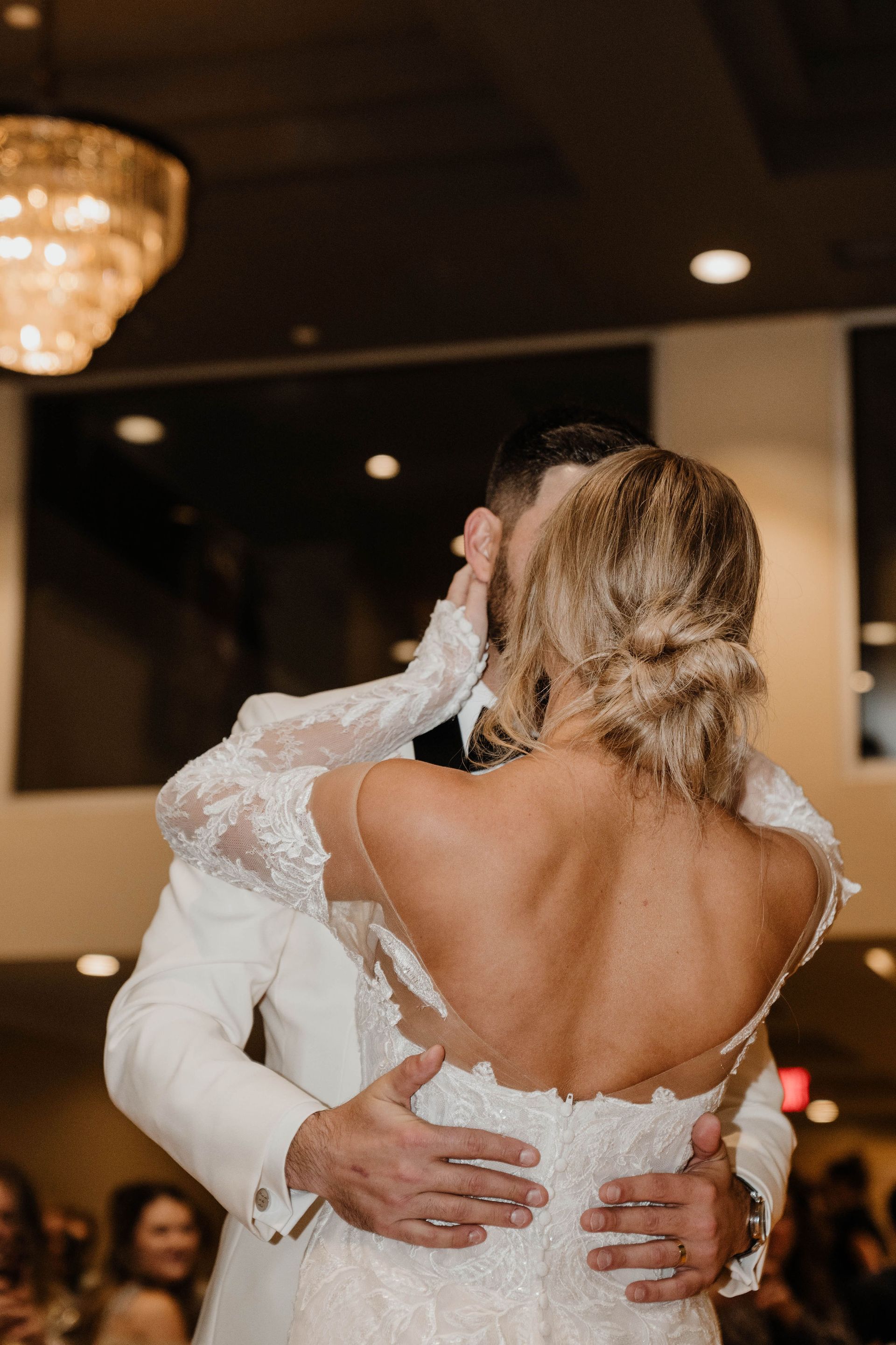 Couple dancing at wedding reception. The bride in a lace backless dress, the groom in a white suit.