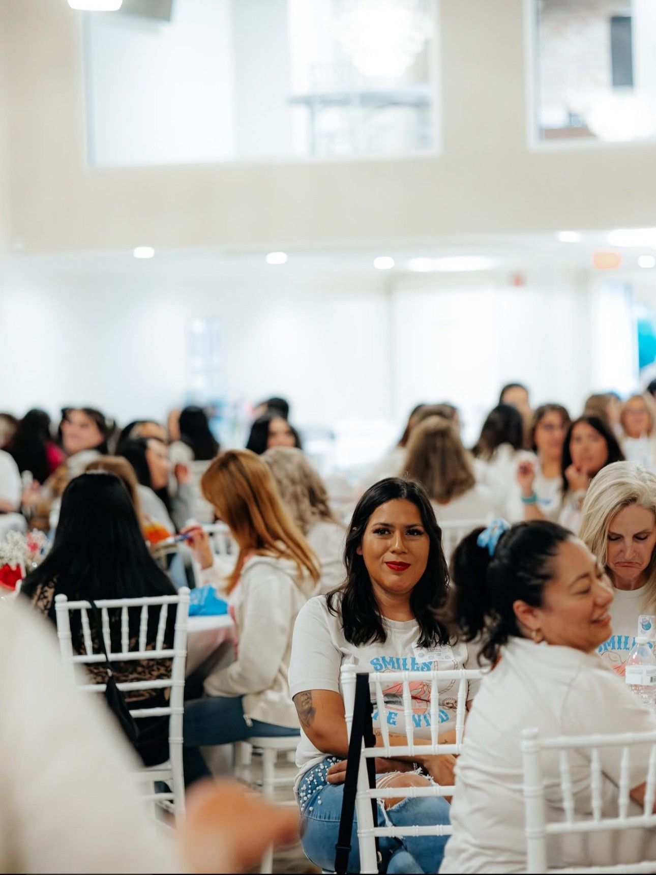 People seated at tables in a bright room, some looking at the camera.