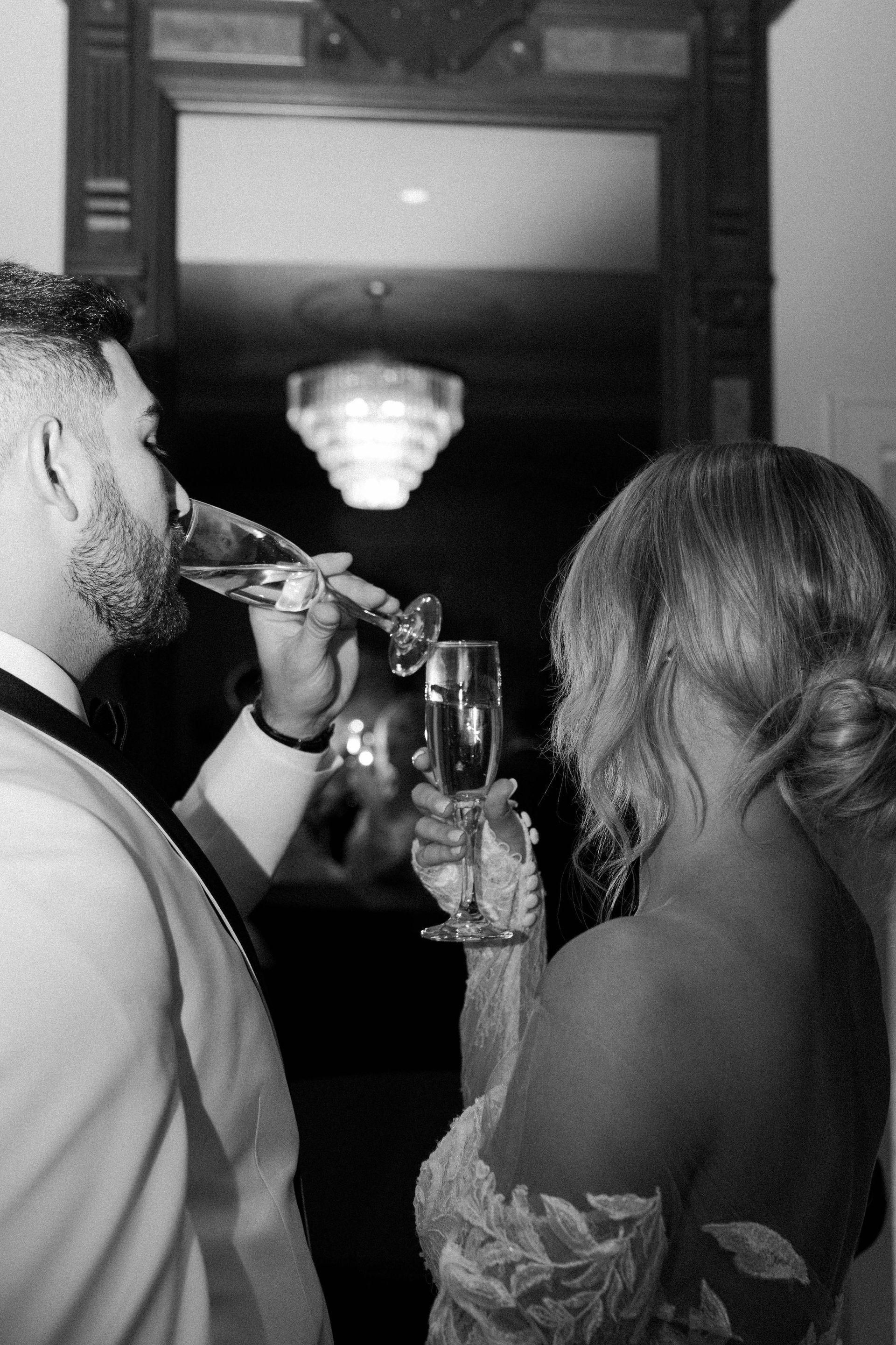 Couple toasting champagne flutes. Formal attire, mirror reflection, chandelier in background.