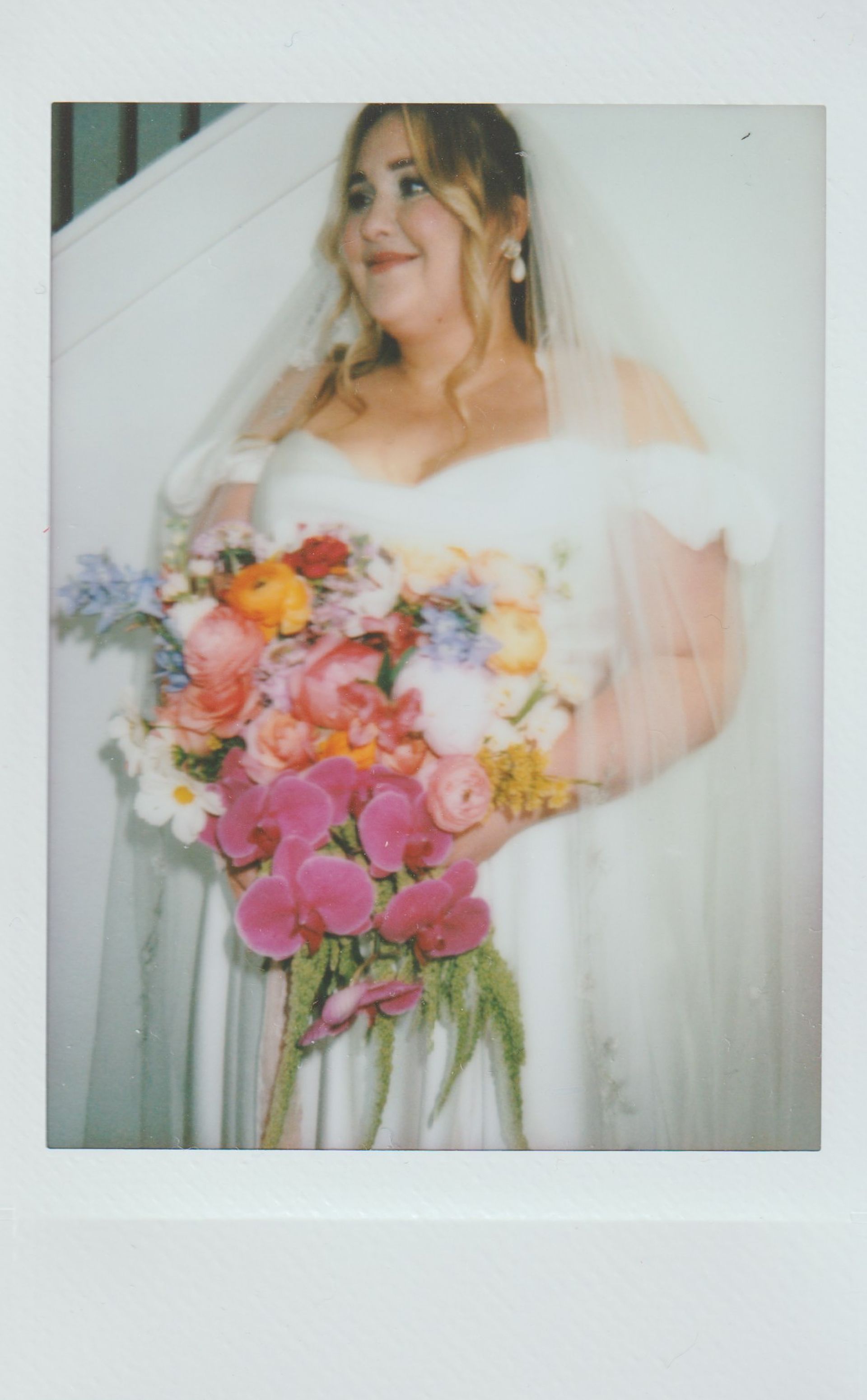 Bride in white dress holding colorful bouquet, smiling, veil over hair.