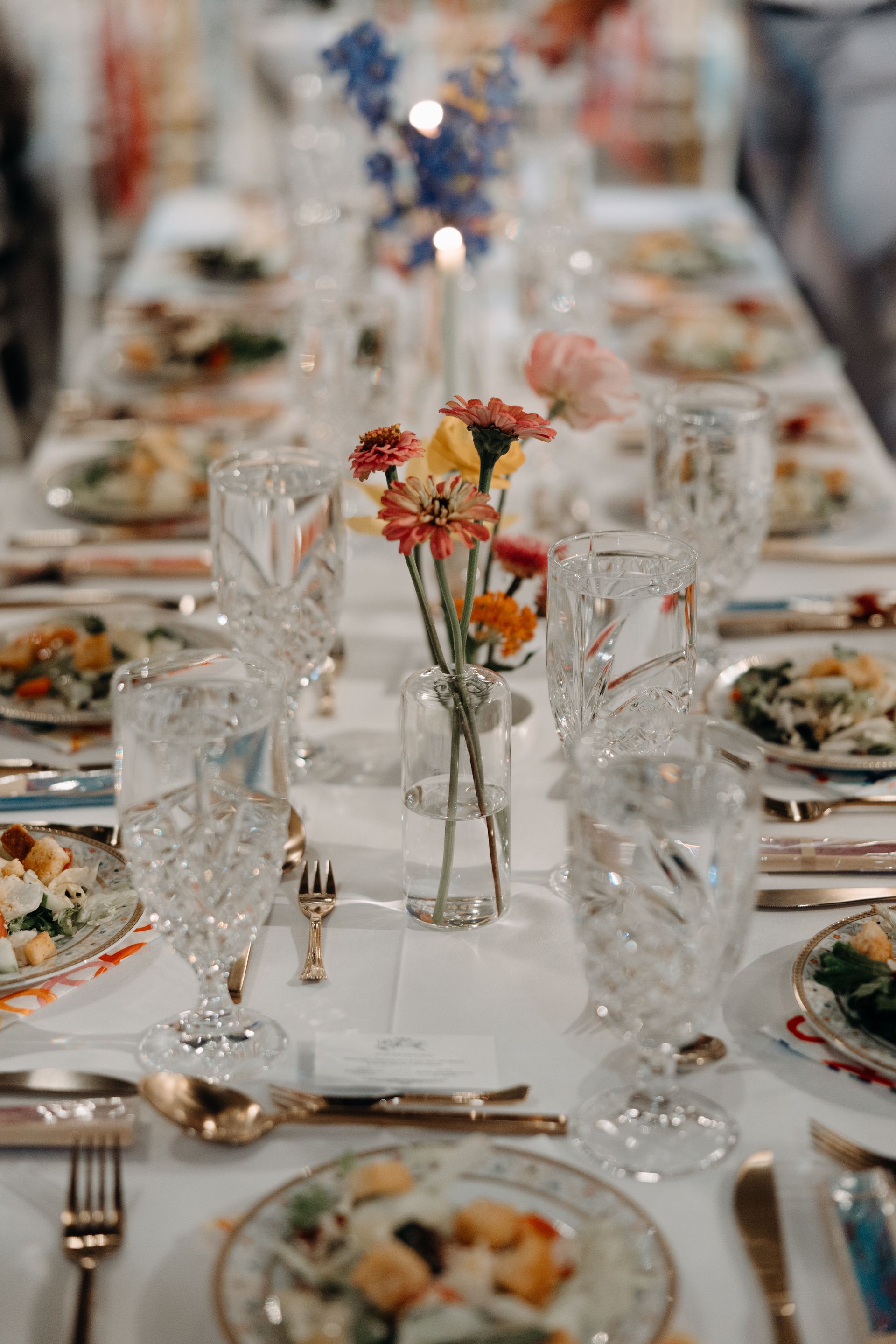 Elegant table setting with crystal glasses, colorful flowers, and plates of food.