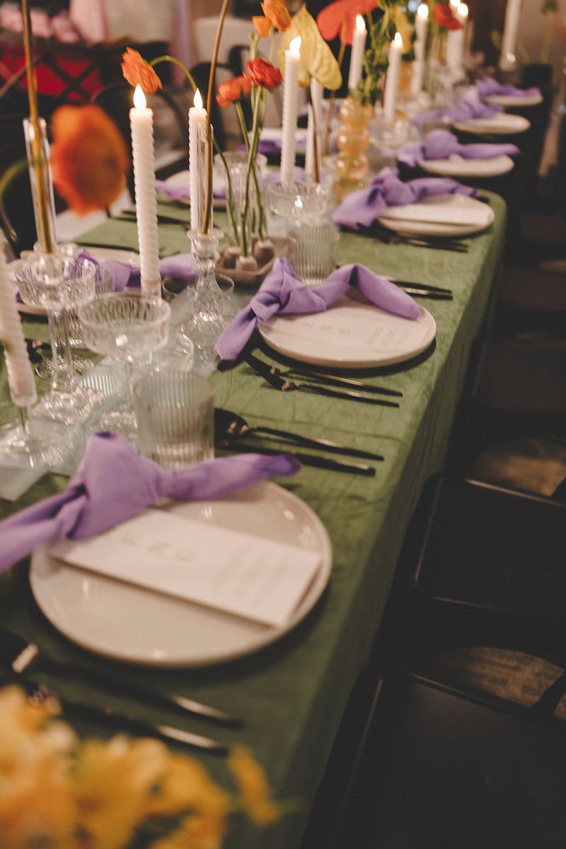 Formal table setting with green tablecloth, white plates, purple napkins, and floral centerpieces.