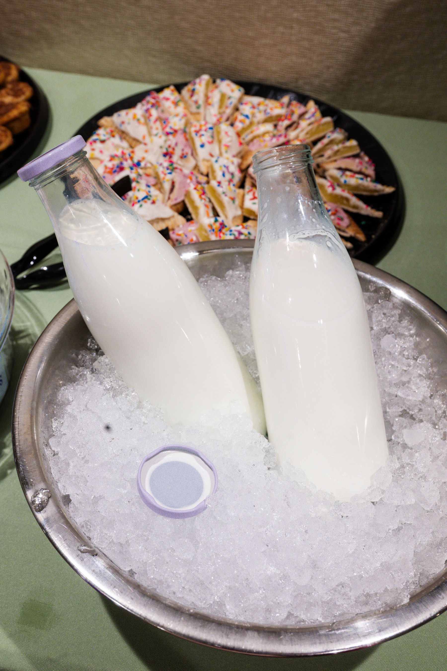 Two glass milk bottles in ice, with frosted sugar cookies in the background.