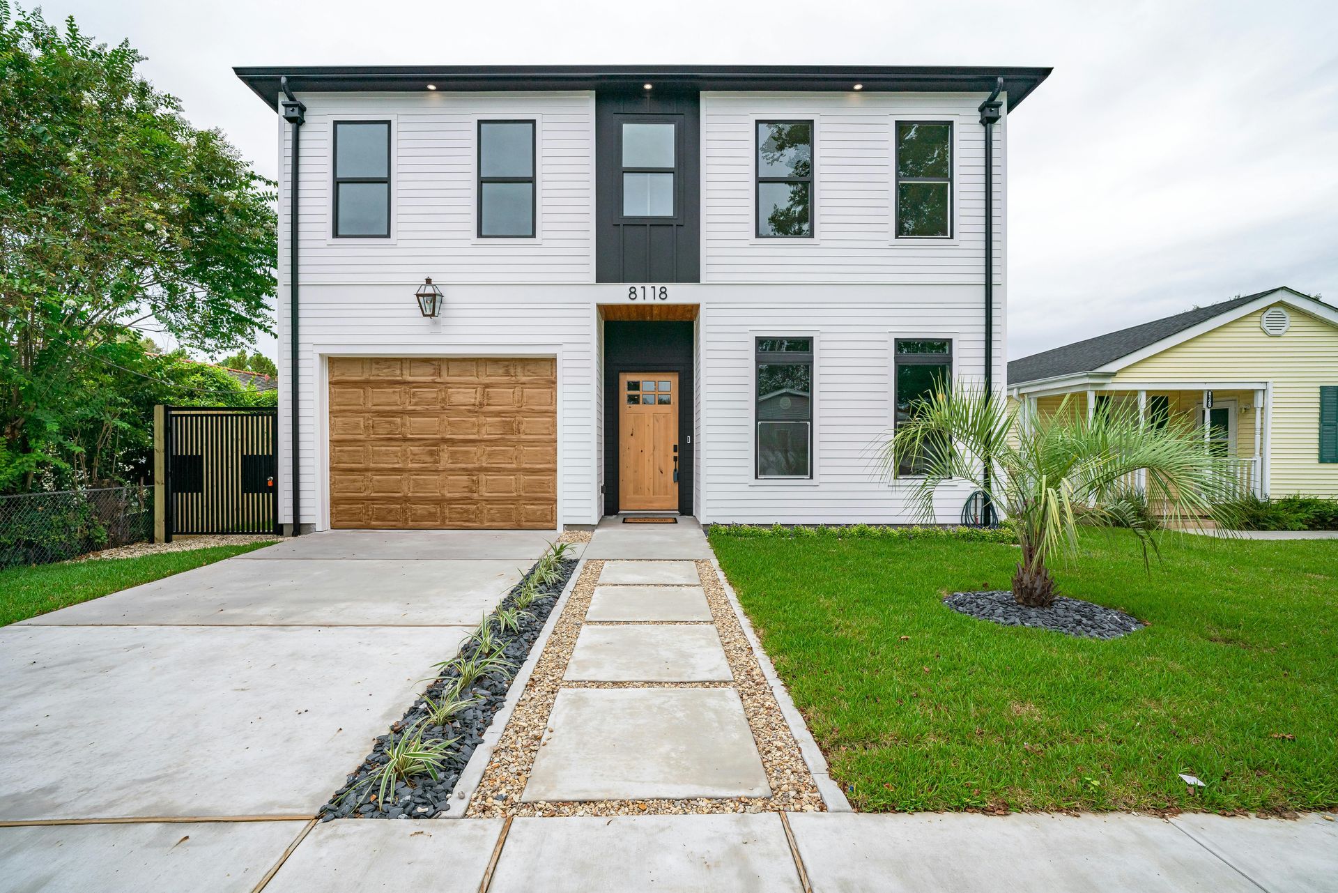 A white house with a wooden garage door and a concrete walkway leading to it.