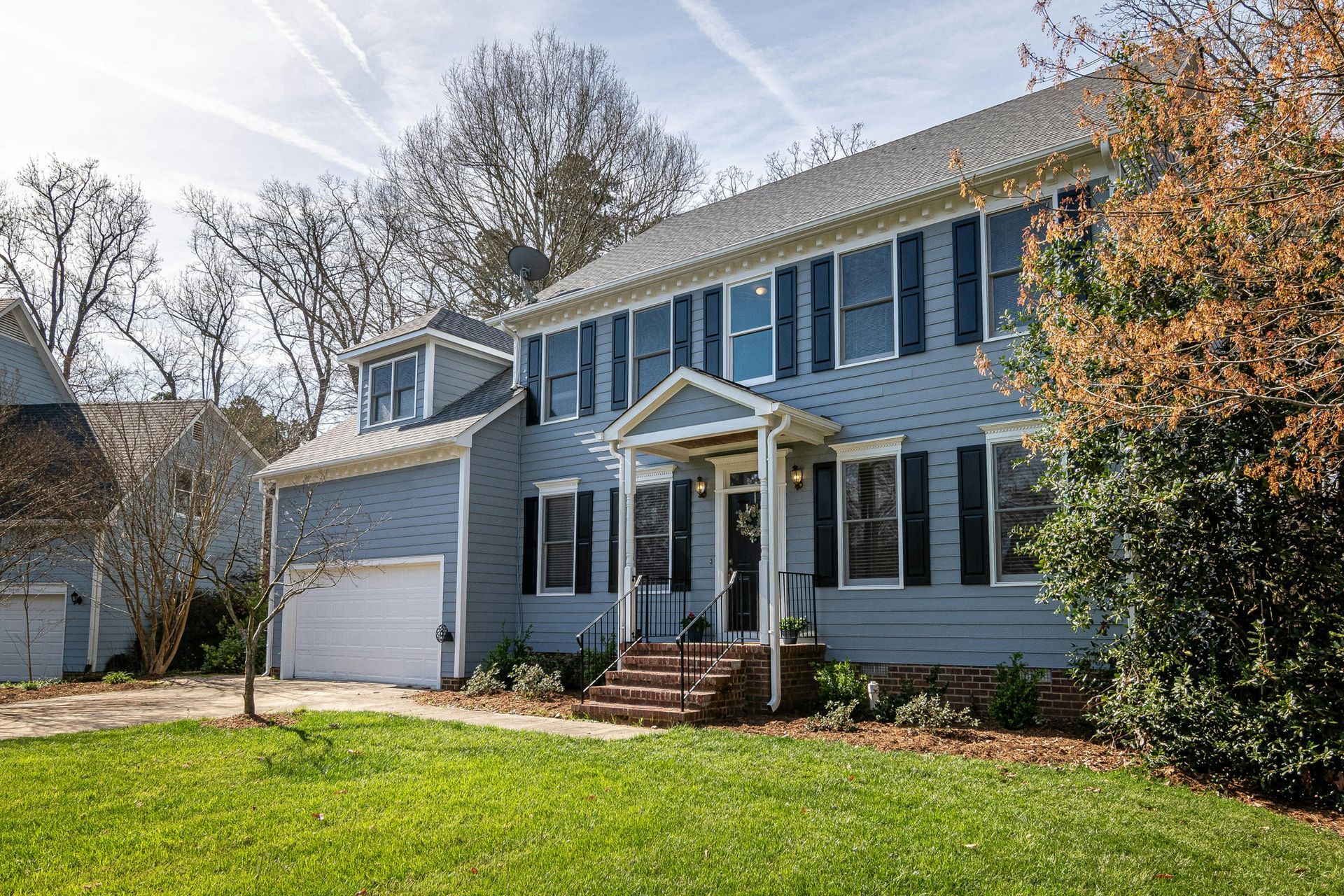 A large blue house with black shutters is sitting on top of a lush green lawn.