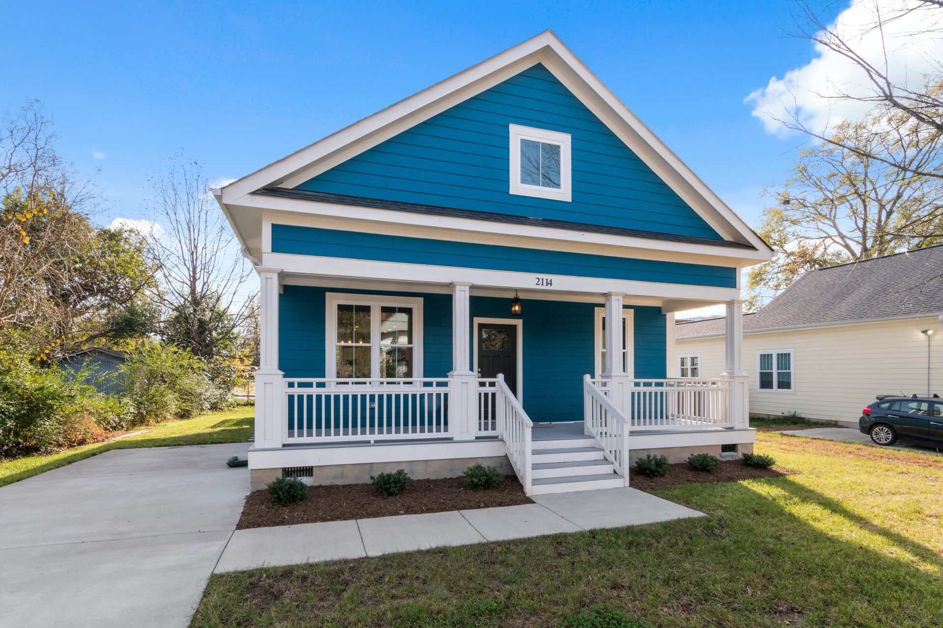 A blue house with a white porch and a car parked in front of it.