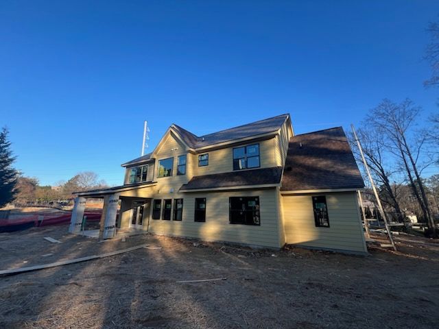 Two-story house under construction with brown roof, green siding, and black windows, under a clear blue sky.