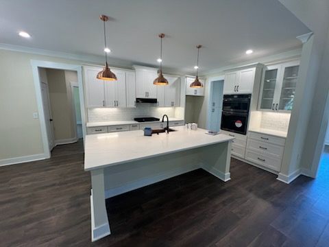 Modern kitchen with white cabinets, island, and copper pendant lights. Dark wood floors.