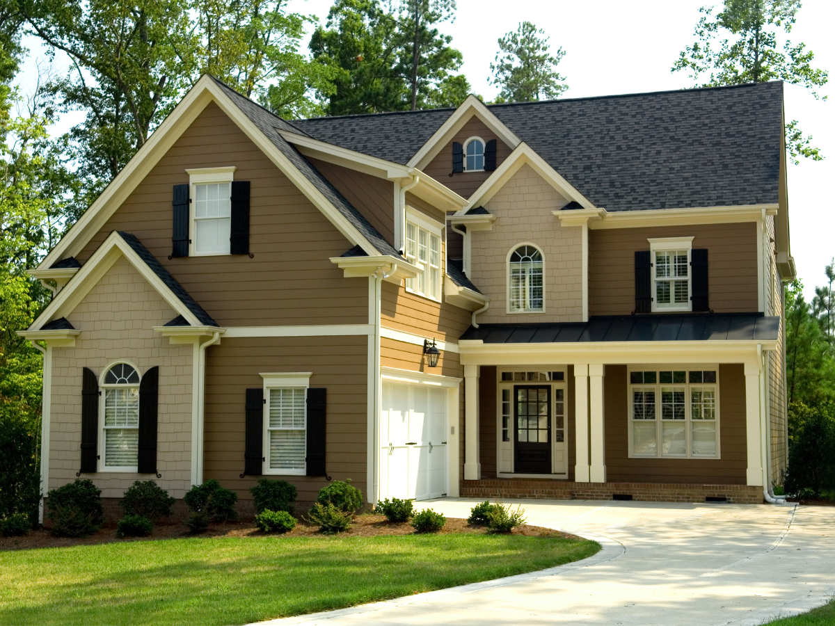 Two-story house with brown and beige siding, black shutters, and a white garage door.