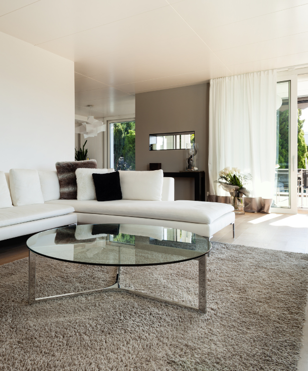 Modern living room with white sofa, glass coffee table, and sheer curtains.