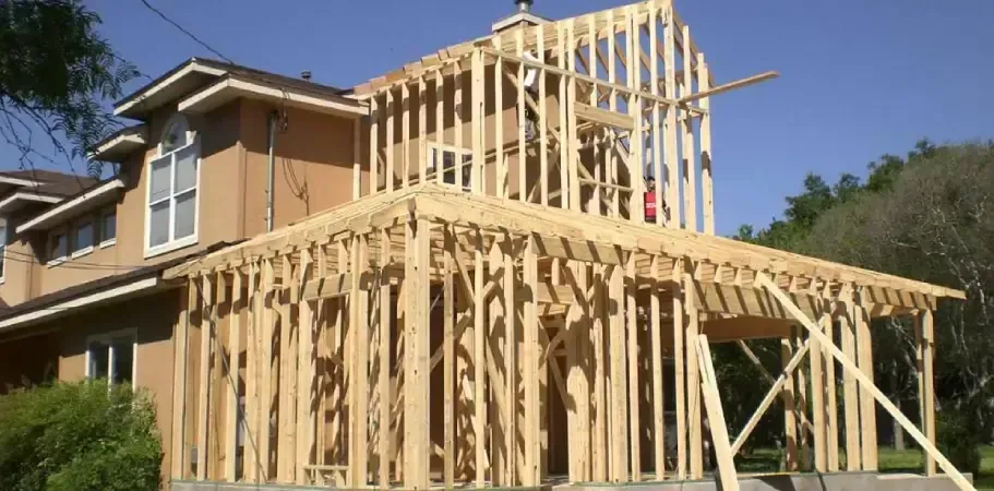 House under construction, framing visible. New porch and second story addition. Clear blue sky.